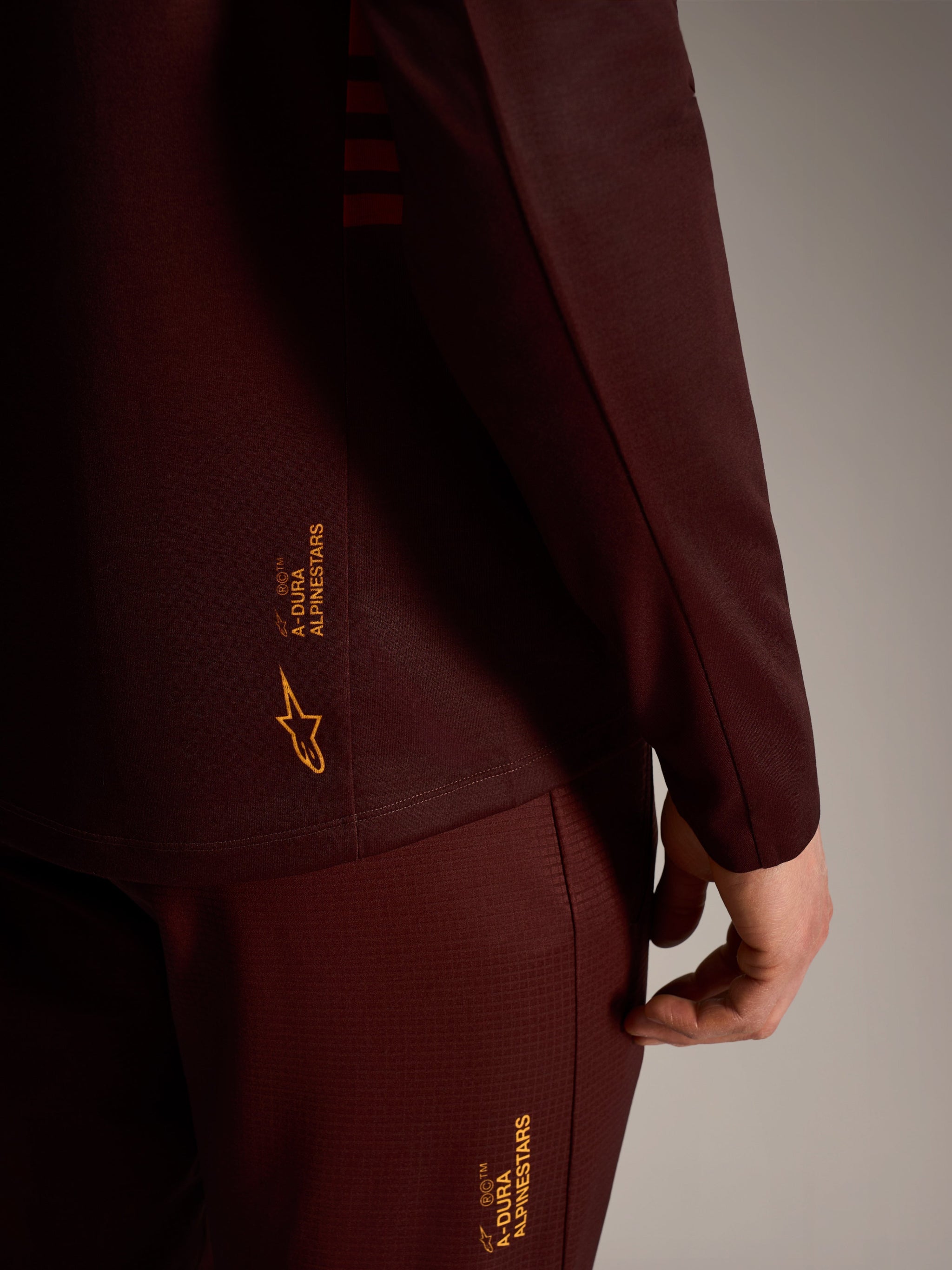 A-Dura Elite trui met lange mouwen in bordeaux, met gele Alpinestars-branding, technische trail-prestatiekleding.