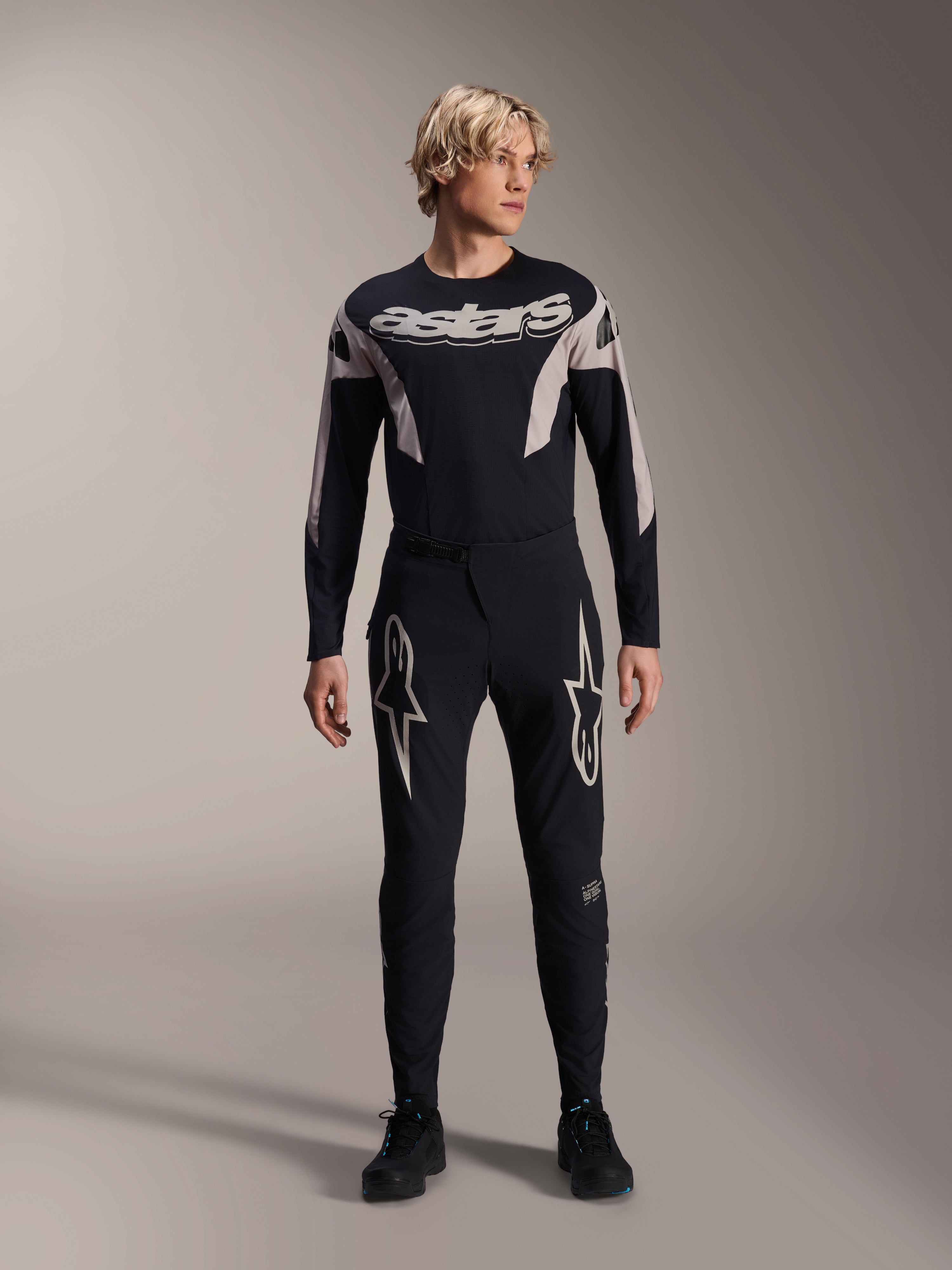 Pantalon Alpinestars A-Supra Melt et maillot à manches longues assorti, mannequin portant une tenue de VTT noire avec de grands graphismes d'étoiles blanches sur les cuisses et marquage 'astars' sur la poitrine, équipement de VTT professionnel