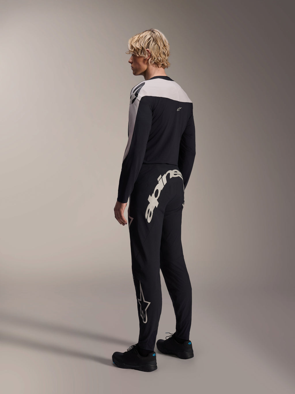 Pantalon Alpinestars A-Supra Melt, pantalon de VTT, noir, avec un grand logo Alpinestars blanc sur l'empiècement arrière et le logo étoile sur la jambe, porté par un mannequin avec un maillot à manches longues assorti et des chaussures noires, vue de dos