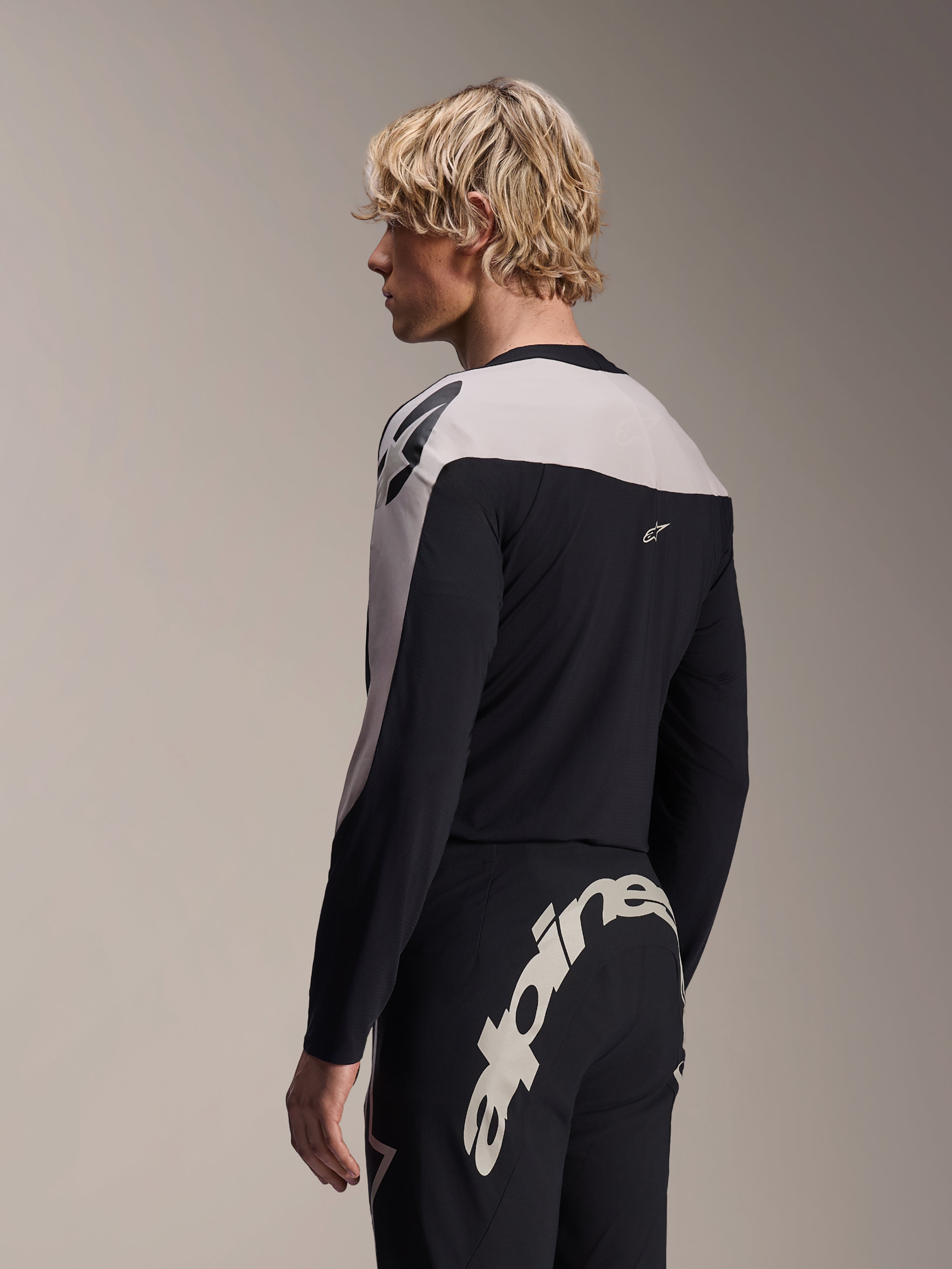 Mannequin homme portant le maillot à manches longues Alpinestars A-Supra Melt et le pantalon A-Supra Melt, tenue de course VTT noir et gris clair, avec un grand marquage Alpinestars blanc sur l'empiècement arrière du pantalon
