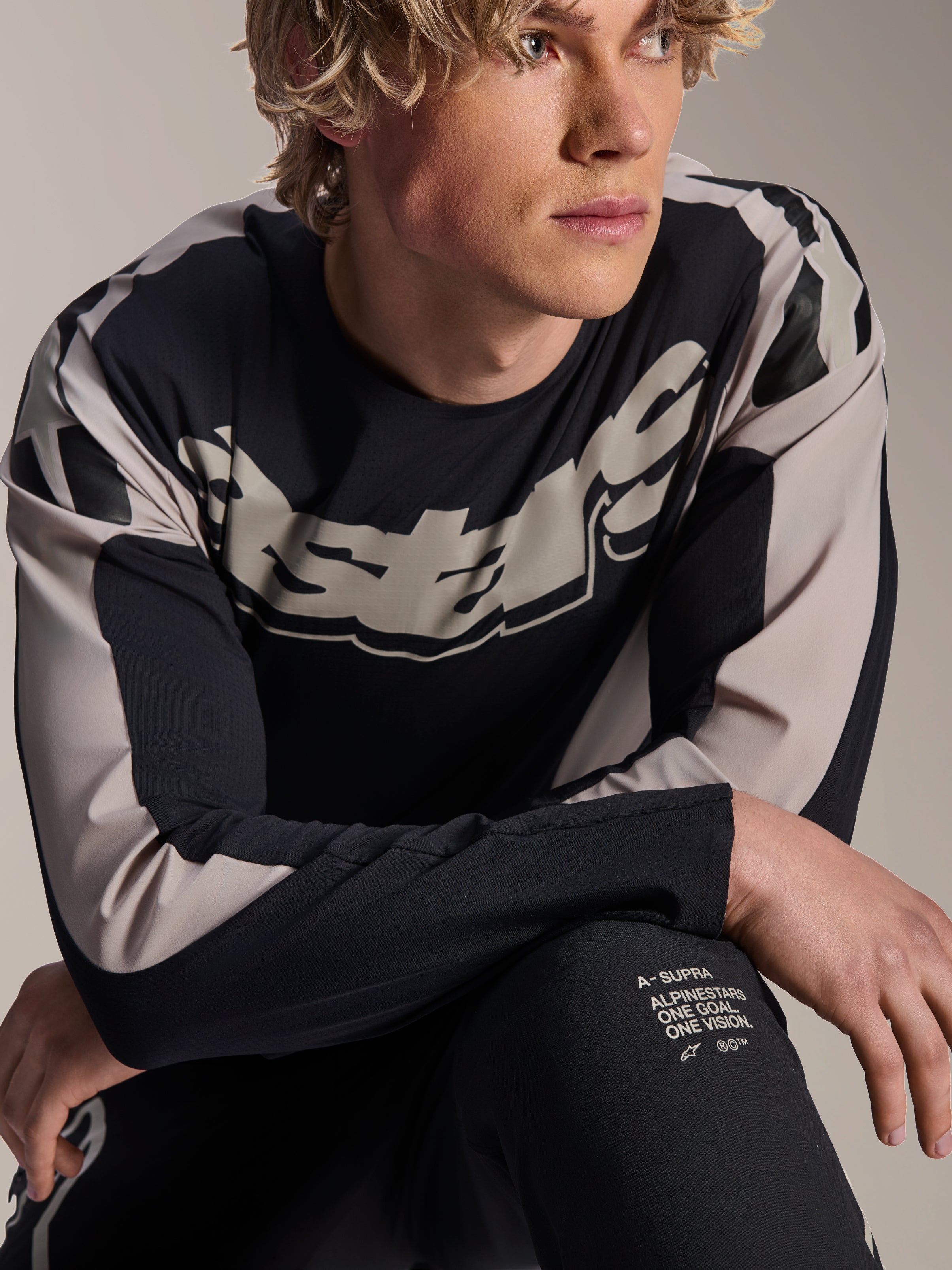 Maillot Alpinestars A-Supra Melt, maillot de VTT à manches longues, noir avec graphismes gris clair, porté par un mannequin, arborant un logo imposant sur la poitrine et l'inscription « One Goal. One Vision. », vêtement de performance pour le VTT