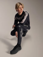 Pantalon et maillot à manches longues Alpinestars A-Supra Melt, noir et gris, avec logos blancs et logos Astars audacieux, portés par un mannequin masculin dans une pose accroupie, tenue de course VTT coordonnée