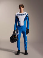 Modèle masculin portant la tenue de VTT Alpinestars A-Supra Melt, maillot à manches longues blanc et bleu avec marquage "astars", pantalon A-Supra Melt bleu avec logo blanc, casque intégral noir, gants et chaussures noirs, équipement de cyclisme tout-terrain coordonné