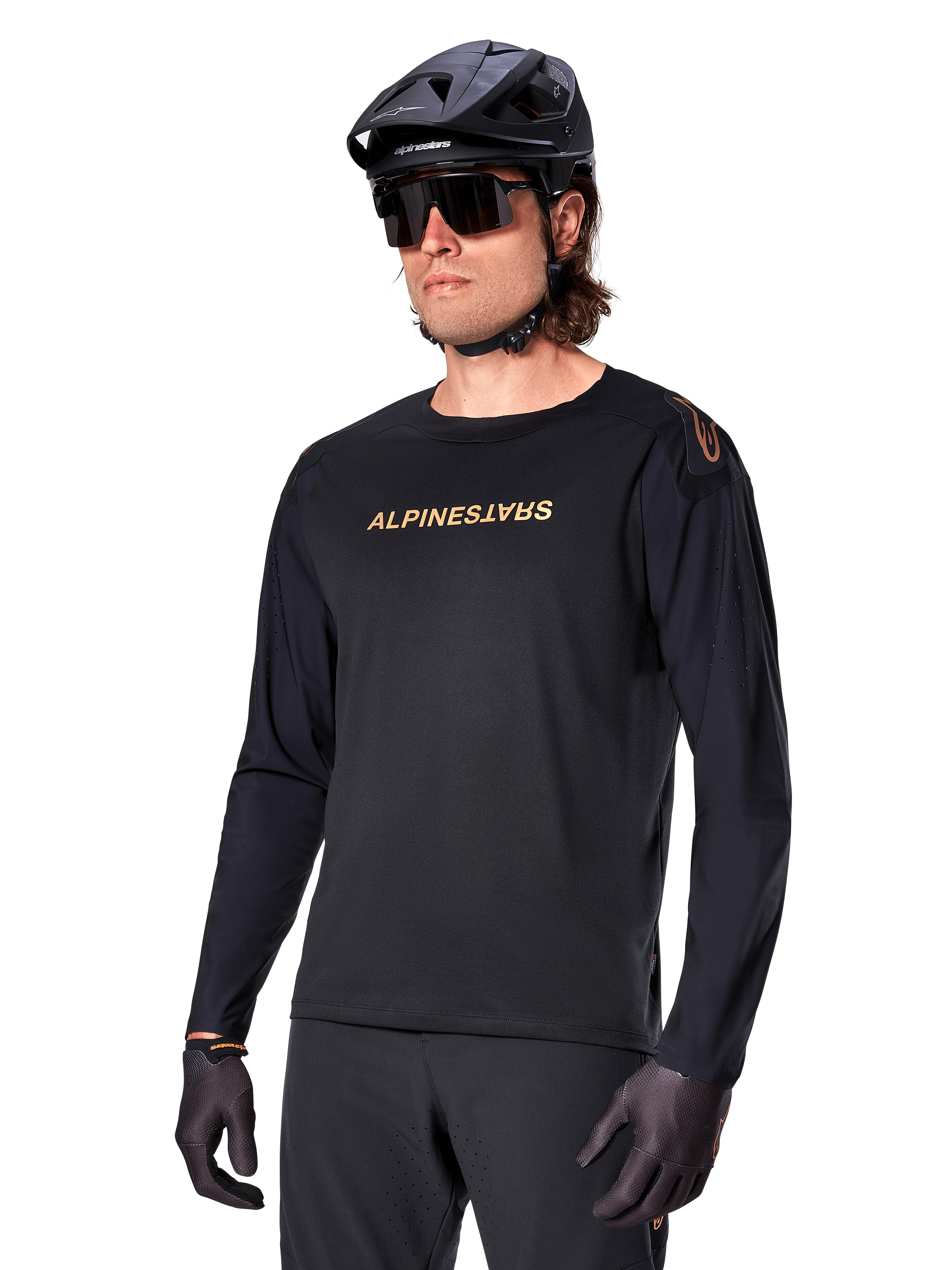 Maillot à manches longues Alpinestars A-Aria Polartec Switch, noir avec logo doré, vêtement de VTT, porté avec un casque noir et des lunettes de soleil, doté de ventilations découpées au laser sur les manches et d'un tissu Polartec évacuant l'humidité pour des performances tout-terrain