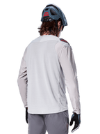 Maillot à manches longues Alpinestars A-Aria Polartec Switch, gris clair, vue de dos sur un cycliste, porté avec un casque de VTT bleu et un pantalon gris, vêtement de VTT performant pour les sentiers tout-terrain