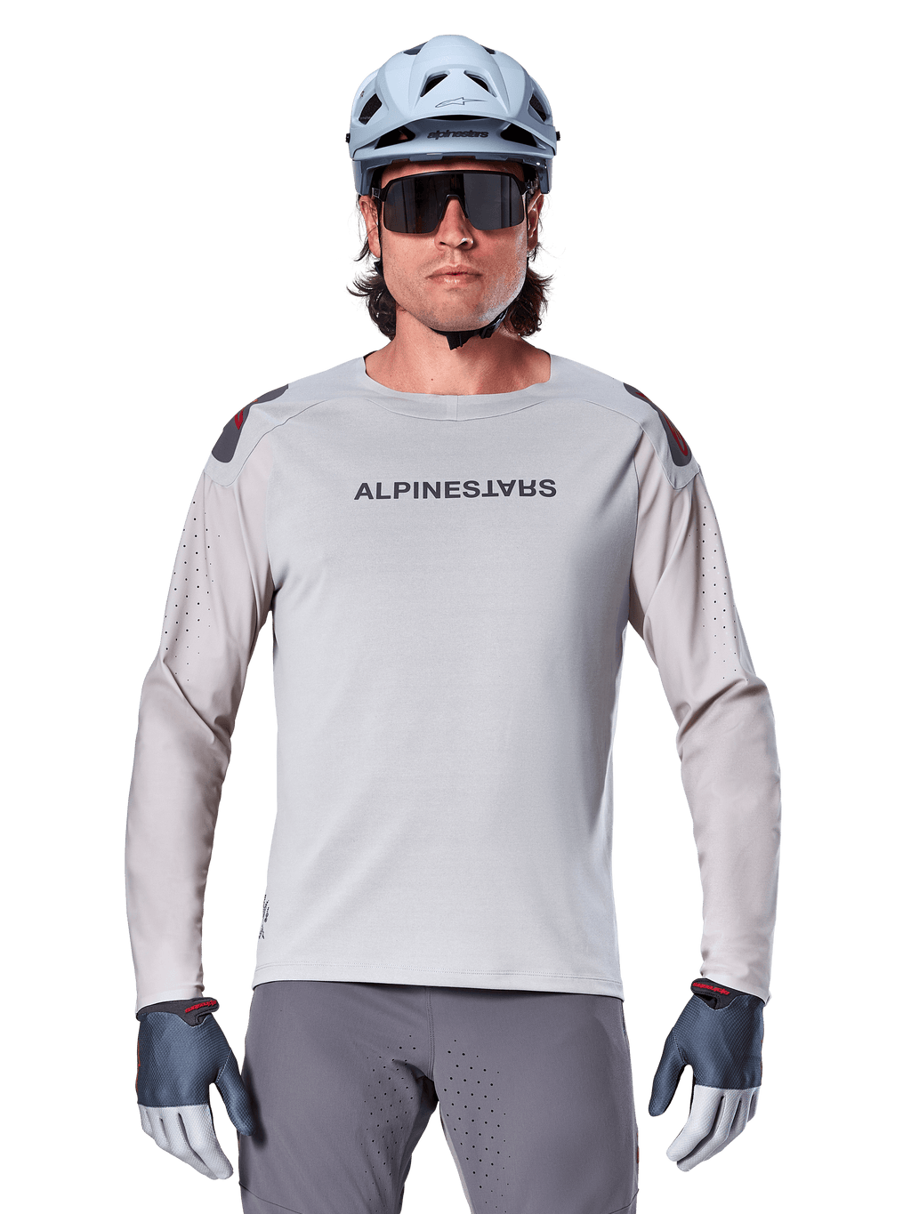 Maillot à manches longues Alpinestars A-Aria Polartec Switch, maillot de VTT gris clair avec perforations laser sur les manches et marquage sur la poitrine, porté avec un casque bleu clair, des lunettes de soleil et des gants gris