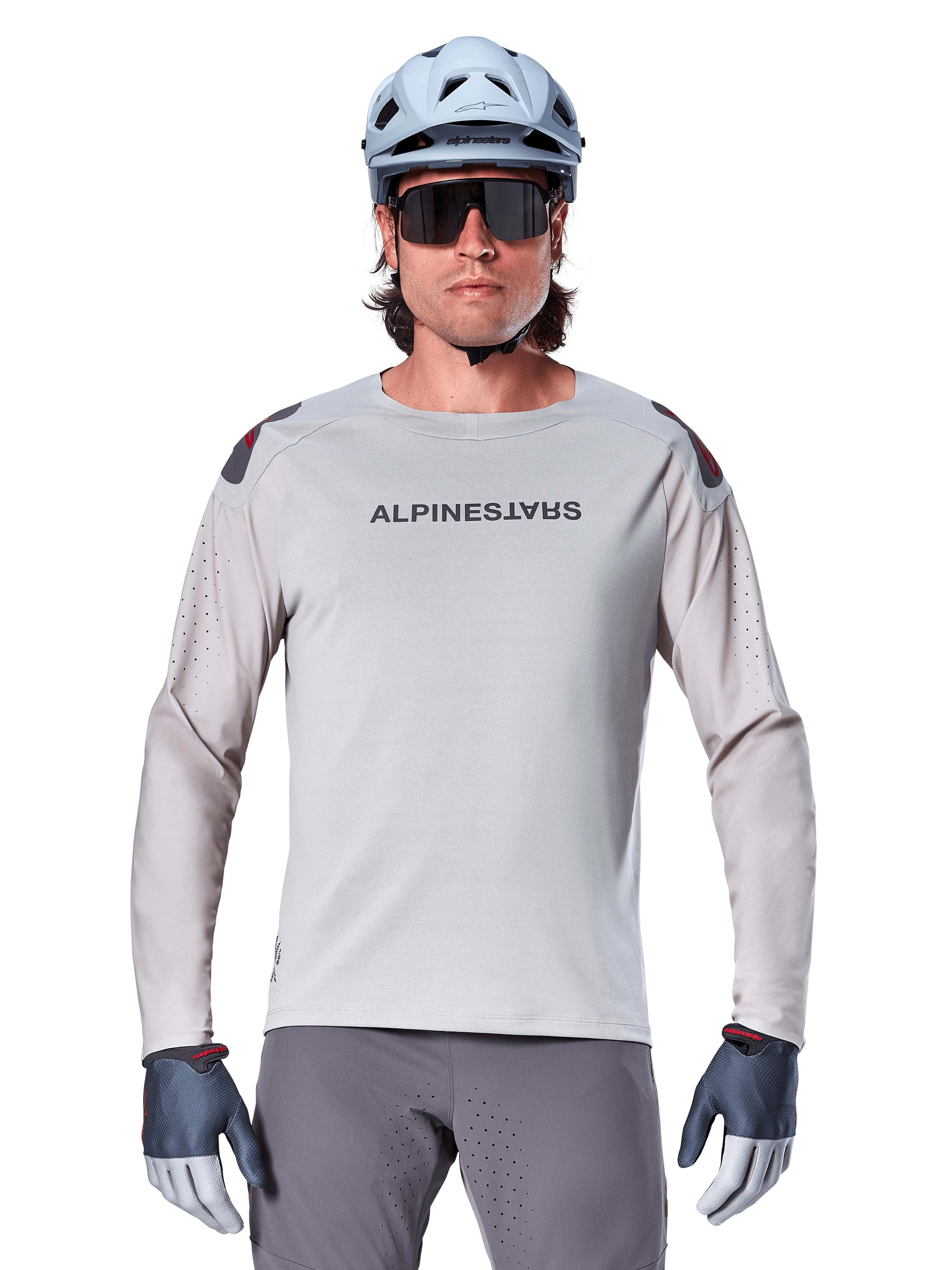 Maillot à manches longues Alpinestars A-Aria Polartec Switch, maillot de VTT gris clair avec perforations laser sur les manches et marquage sur la poitrine, porté avec un casque bleu clair, des lunettes de soleil et des gants gris