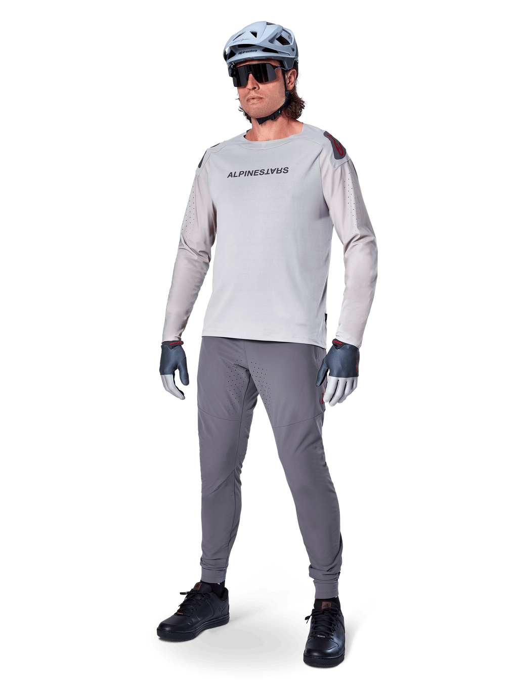 Maillot Alpinestars A-Aria Polartec Switch, maillot de VTT à manches longues, gris clair, porté avec un pantalon de VTT gris foncé, un casque et des gants, avec des manches perforées au laser et le logo Alpinestars sur la poitrine.