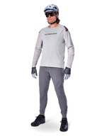 Maillot Alpinestars A-Aria Polartec Switch, maillot de VTT à manches longues, gris clair, porté avec un pantalon de VTT gris foncé, un casque et des gants, avec des manches perforées au laser et le logo Alpinestars sur la poitrine.
