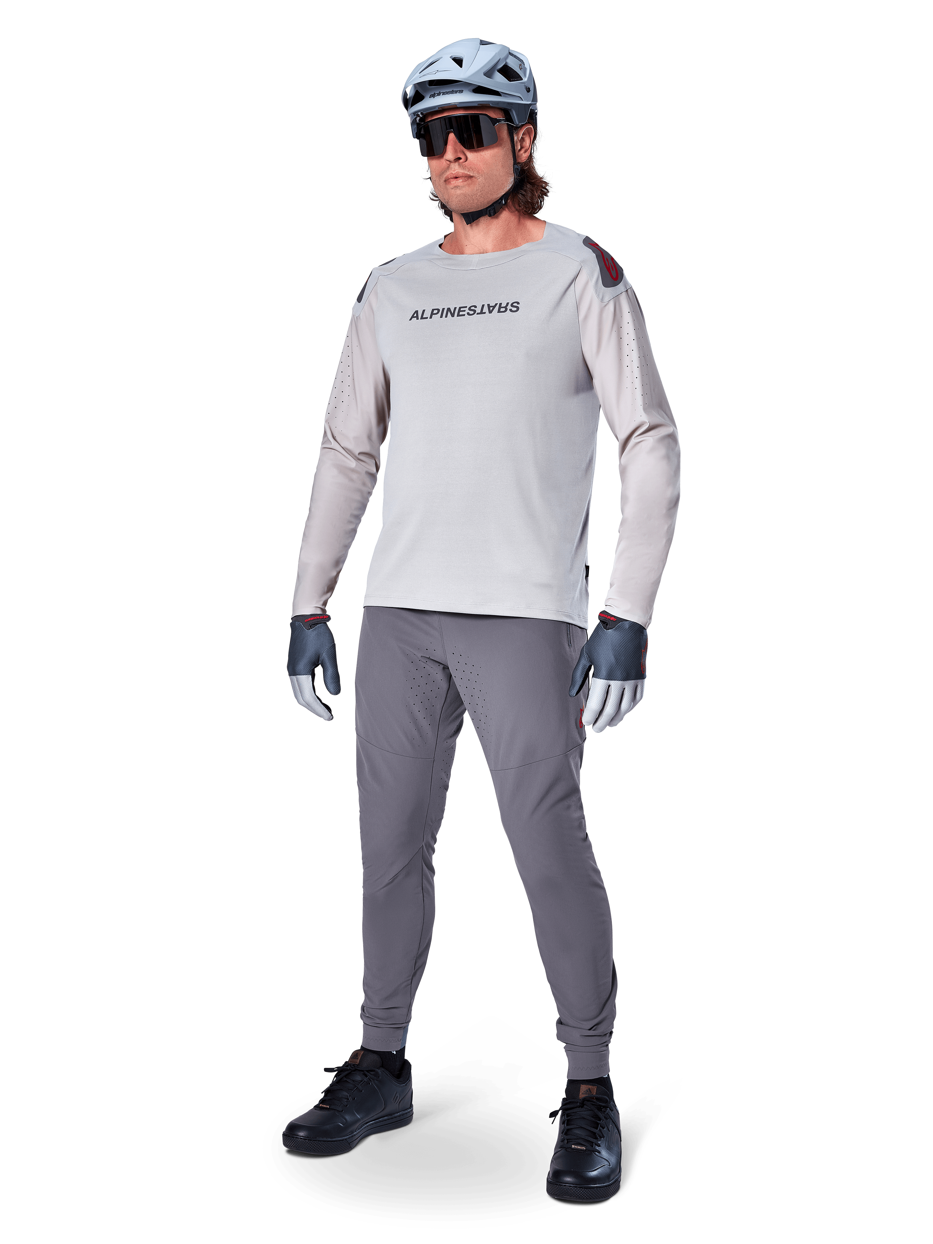 Maillot Alpinestars A-Aria Polartec Switch, maillot de VTT à manches longues, gris clair, porté avec un pantalon de VTT gris foncé, un casque et des gants, avec des manches perforées au laser et le logo Alpinestars sur la poitrine.