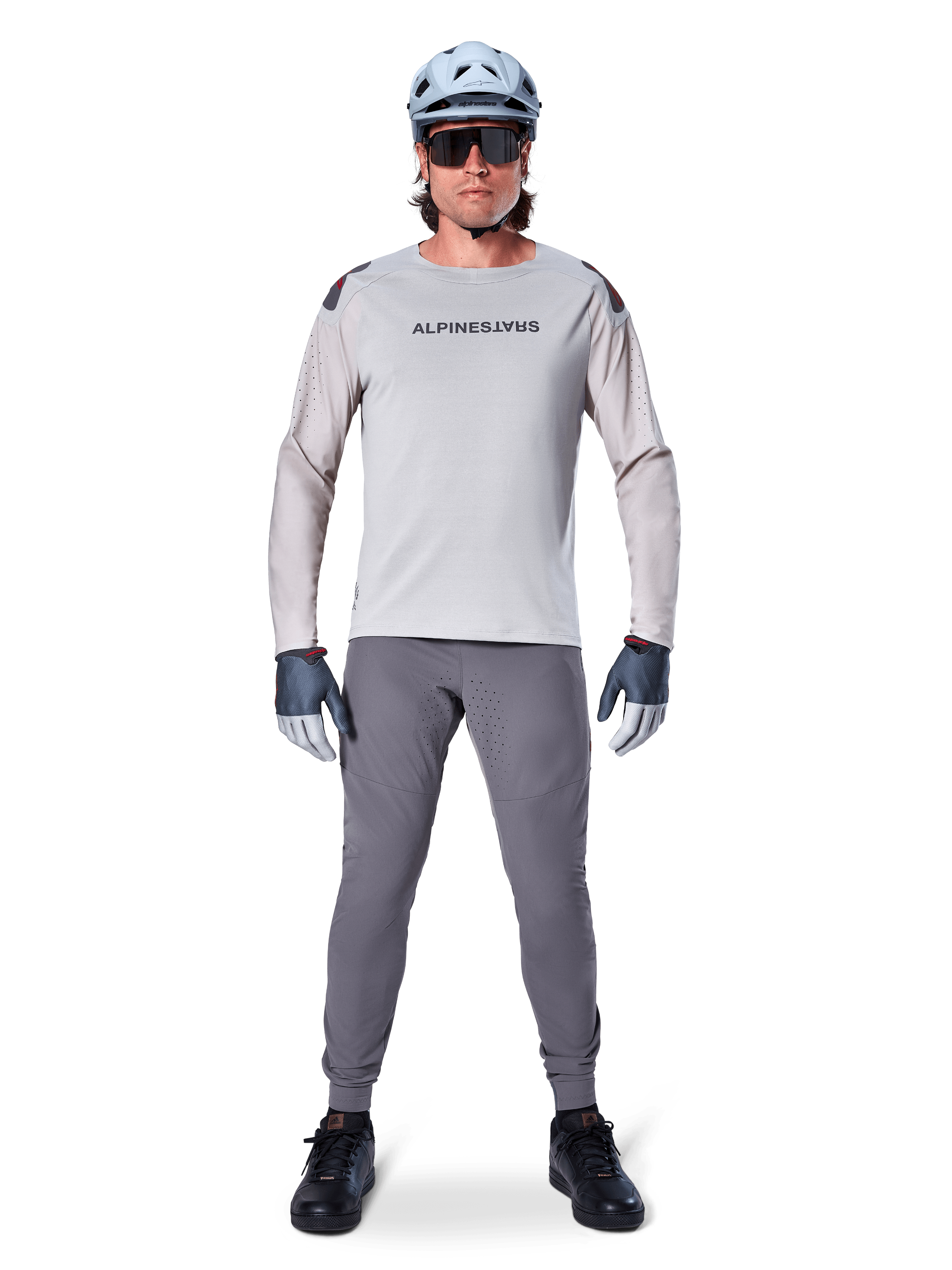 Maillot à manches longues Alpinestars A-Aria Polartec Switch, gris clair, porté par un cycliste de VTT avec pantalon gris foncé, casque bleu clair et lunettes de soleil, avec marquage sur la poitrine et ventilations perforées au laser sur les manches, tenue de cyclisme tout-terrain complète.