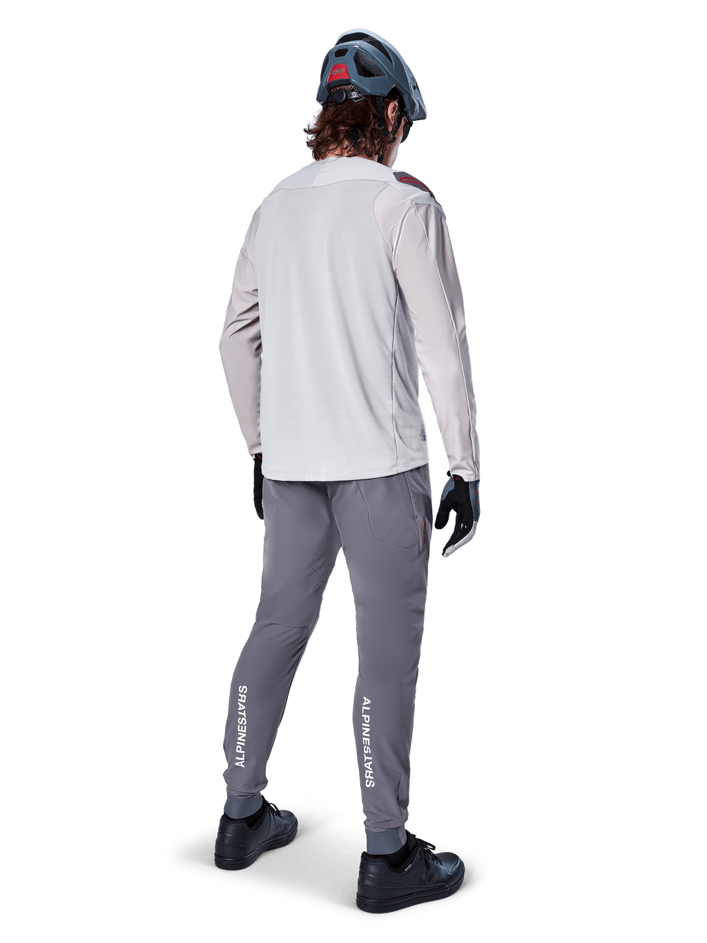 Vue arrière d'un cycliste portant le maillot à manches longues Alpinestars A-Aria Polartec Switch en gris clair, associé à un pantalon de VTT gris foncé avec le logo Alpinestars blanc sur les mollets, des gants noirs et un casque gris.