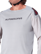 Gros plan sur le maillot à manches longues Alpinestars A-Aria Polartec Switch en gris clair, avec logo Alpinestars sur la poitrine, logo rouge sur l'épaule et manches perforées au laser pour la circulation de l'air, équipement de VTT haut de gamme