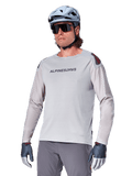 Alpinestars A-Aria Polartec Switch Jersey à manches longues, maillot de cyclisme gris clair avec logo noir sur la poitrine et accent rouge sur l'épaule, manches perforées au laser pour la ventilation, porté avec un casque bleu clair, des lunettes de soleil et un pantalon gris, tenue de VTT haute performance pour le trail