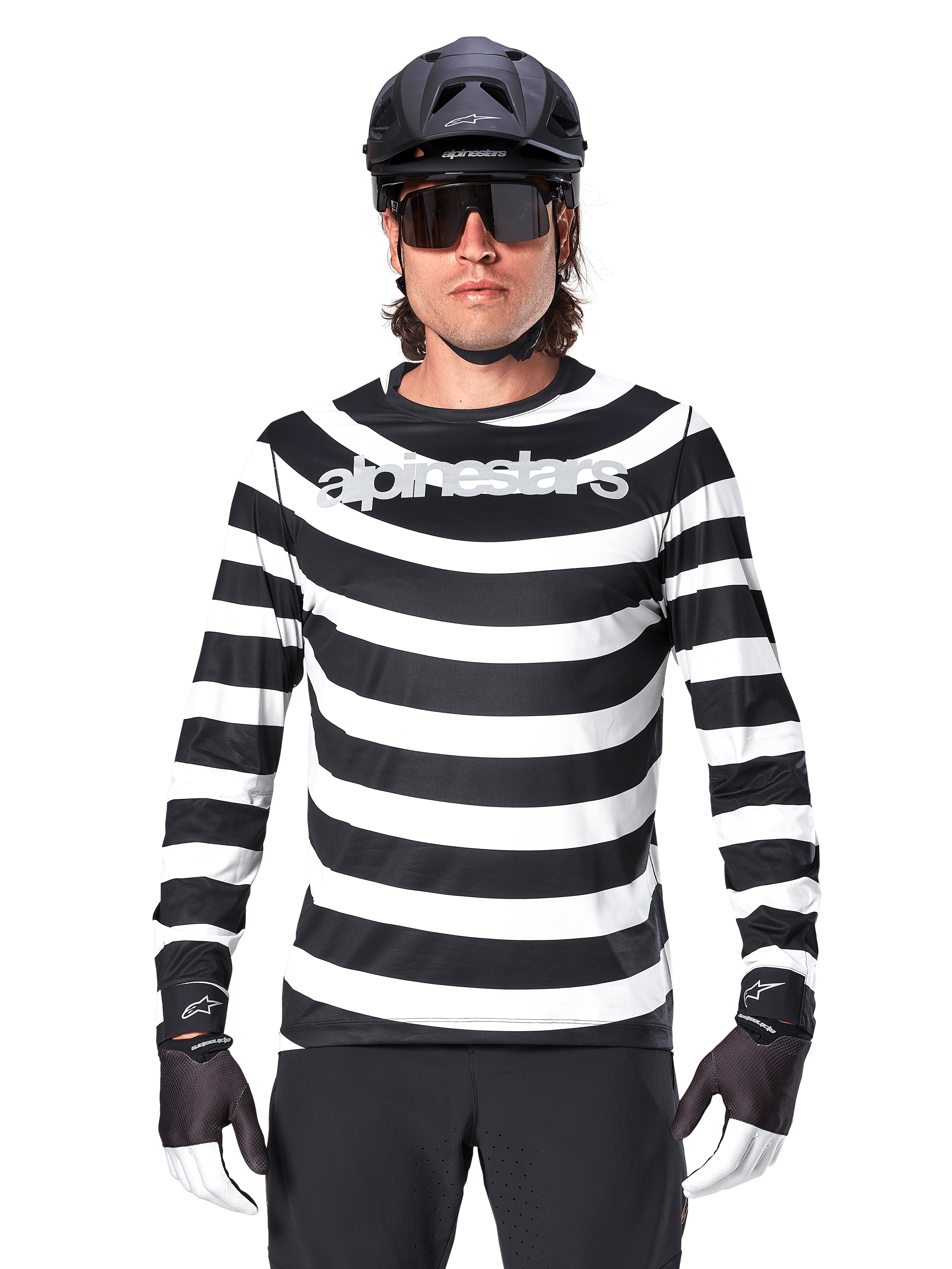 Male cyclist wearing Alpinestars A-Aria Oscar Long Sleeve Jersey, Black and White horizontal stripes, reflective Alpinestars logo on the chest, styled with a black MTB helmet, cycling sunglasses, and performance gloves