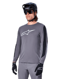 Alpinestars A-Dura Dri Astar Jersey Long Sleeve, donkergrijs met wit logo op de borst en zwarte mesh zijpanelen, MTB mountainbike shirt, gedragen met zwarte helm, zonnebril en bijpassende grijze broek