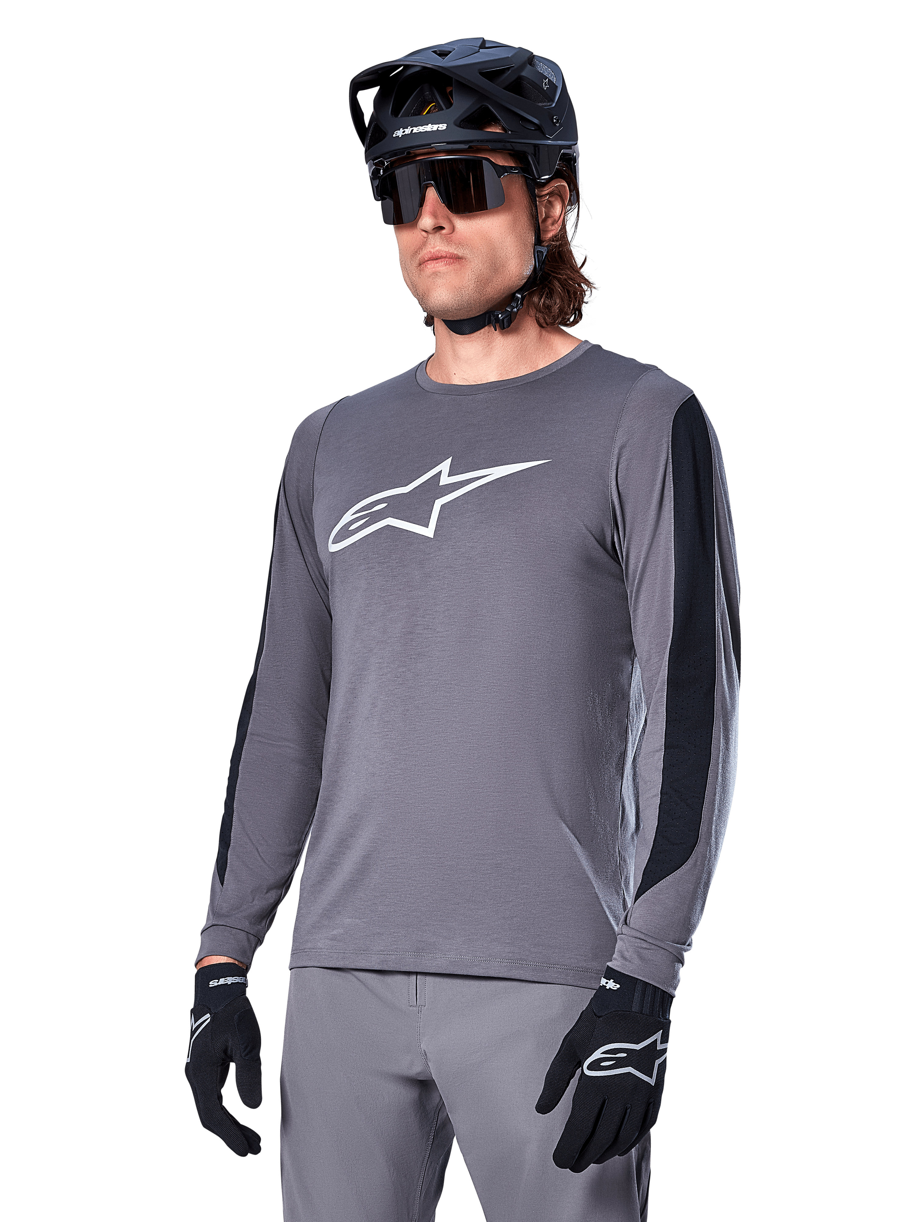 Alpinestars A-Dura Dri Astar Langarmtrikot, MTB-Mountainbike-Trikot, Dunkelgrau mit weißem Brustlogo und schwarzen Mesh-Seiteneinsätzen, getragen mit schwarzem Helm, Sonnenbrille und passender grauer Hose