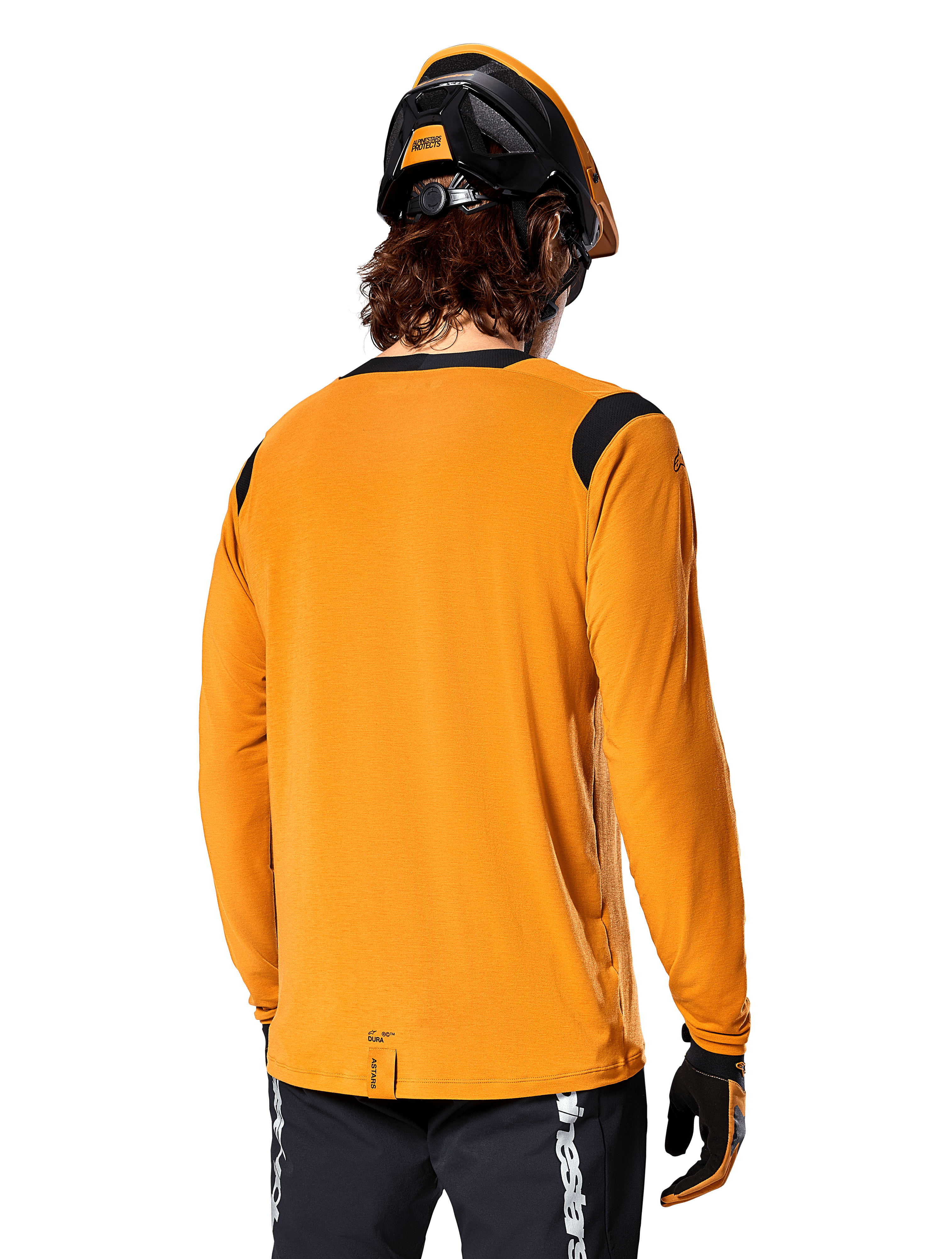 Alpinestars A-Dura Dri Wool Jersey met lange mouwen in Dark Gold, achteraanzicht van een rijder met mountainbikehelm en handschoenen, voorzien van zwarte mesh-panelen op de schouders en een verlengde achterzijde, technische fietskleding voor trailrijden