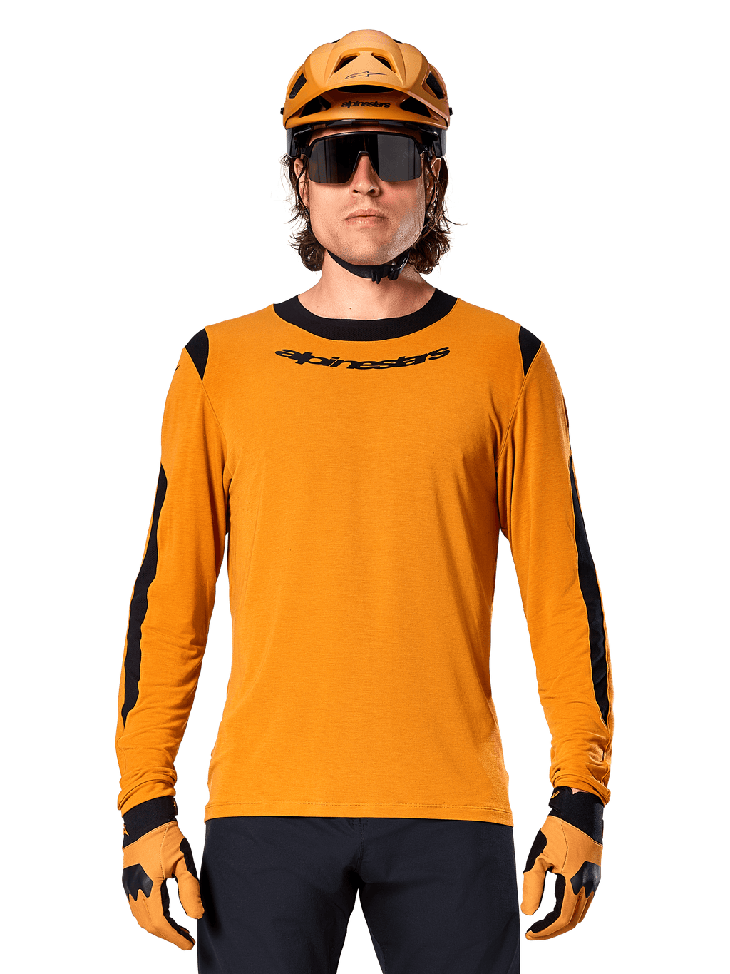 Mannelijk model draagt Alpinestars A-Dura Dri Wool Jersey met lange mouwen in Dark Gold, gecombineerd met een bijpassende gouden MTB-helm en handschoenen, zwarte mesh panelen op schouders en mouwen, zwart Alpinestars-woordmerk op de borst, donkere zonnebril en broek, technische mountainbikekleding