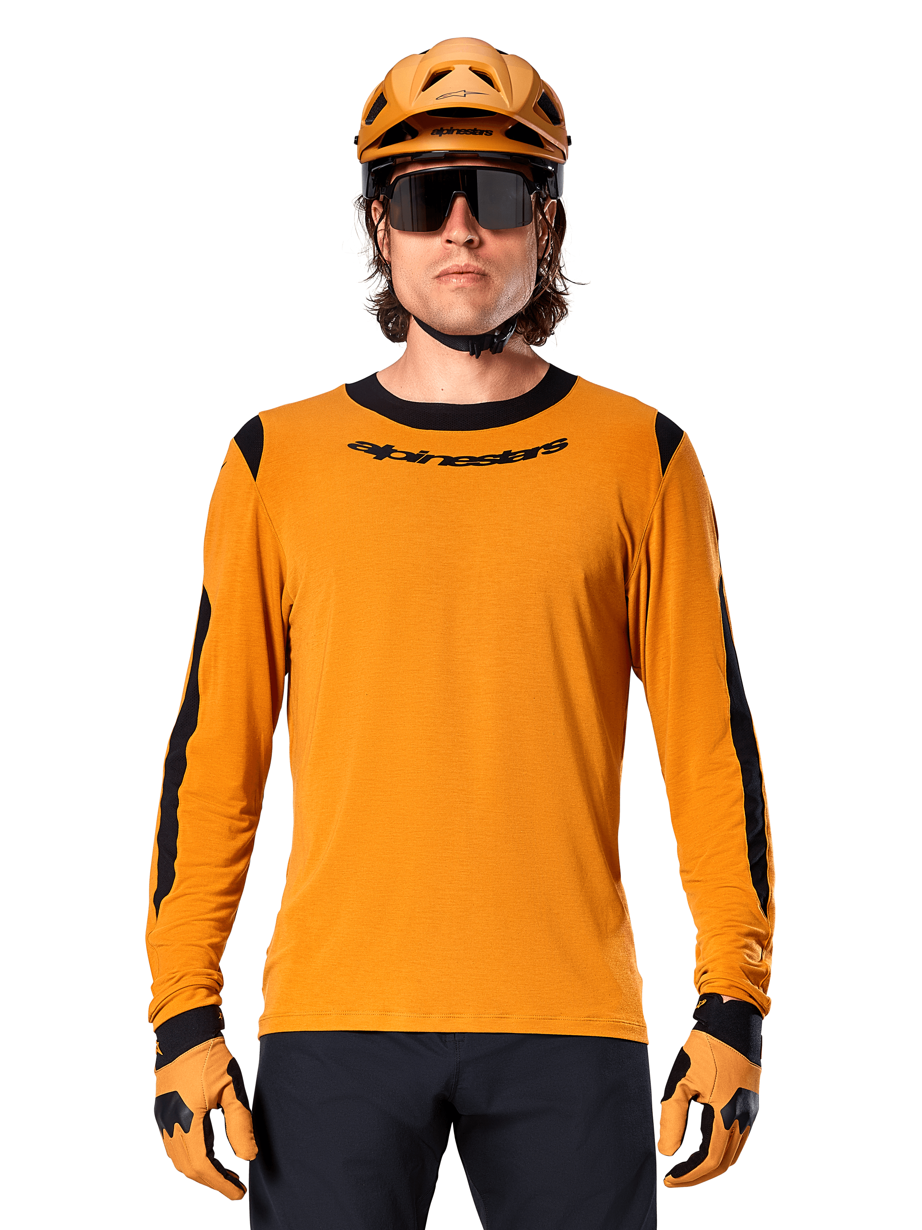 Mannelijk model draagt Alpinestars A-Dura Dri Wool Jersey met lange mouwen in Dark Gold, gecombineerd met een bijpassende gouden MTB-helm en handschoenen, zwarte mesh panelen op schouders en mouwen, zwart Alpinestars-woordmerk op de borst, donkere zonnebril en broek, technische mountainbikekleding