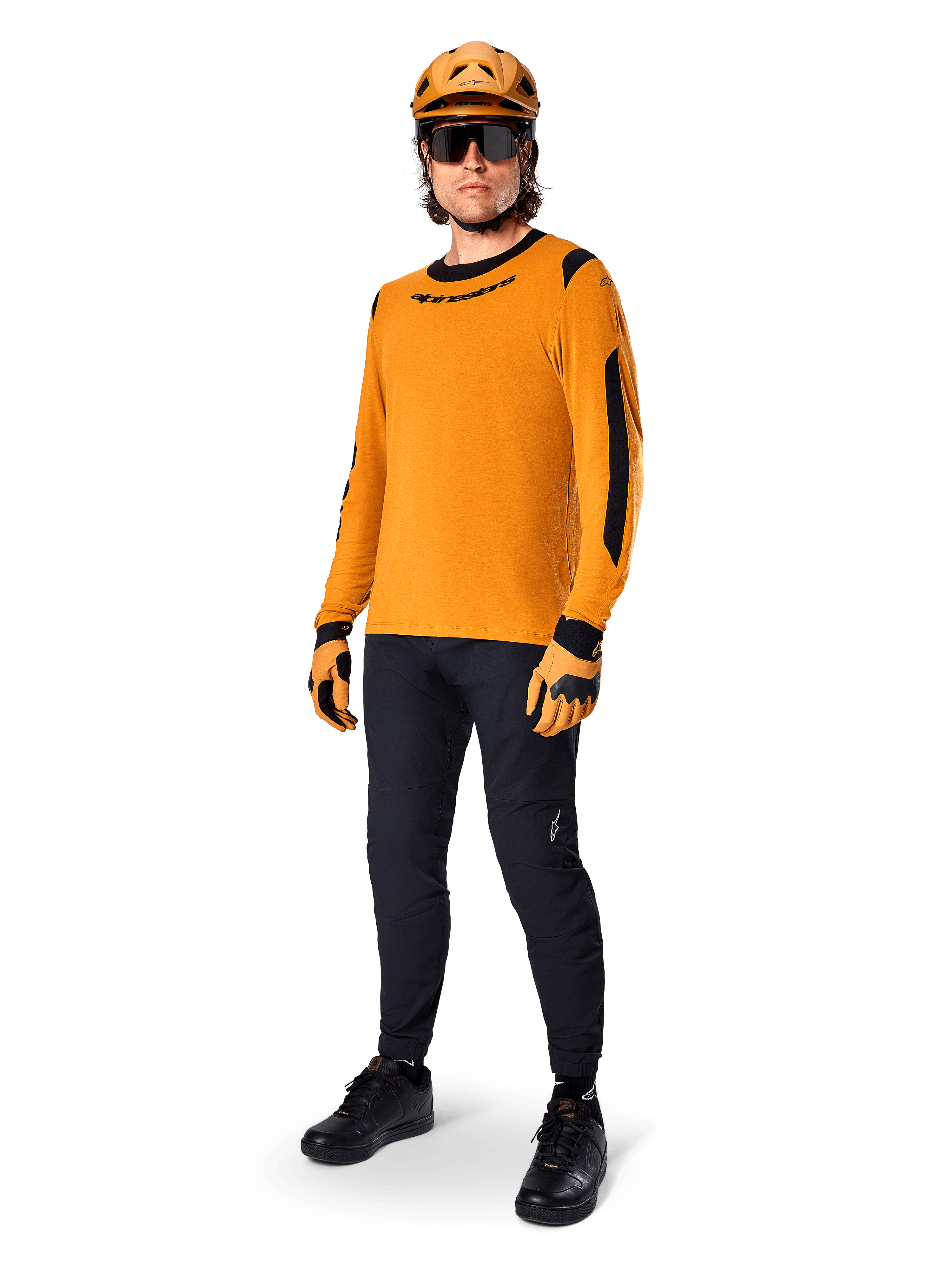 Alpinestars A-Dura Dri Wool Jersey - lange mouwen, donkergoud, gedragen met bijpassende oranje helm, zwarte MTB-broek en geel-zwarte handschoenen, volledige fietsoutfit voor off-road trailrijden