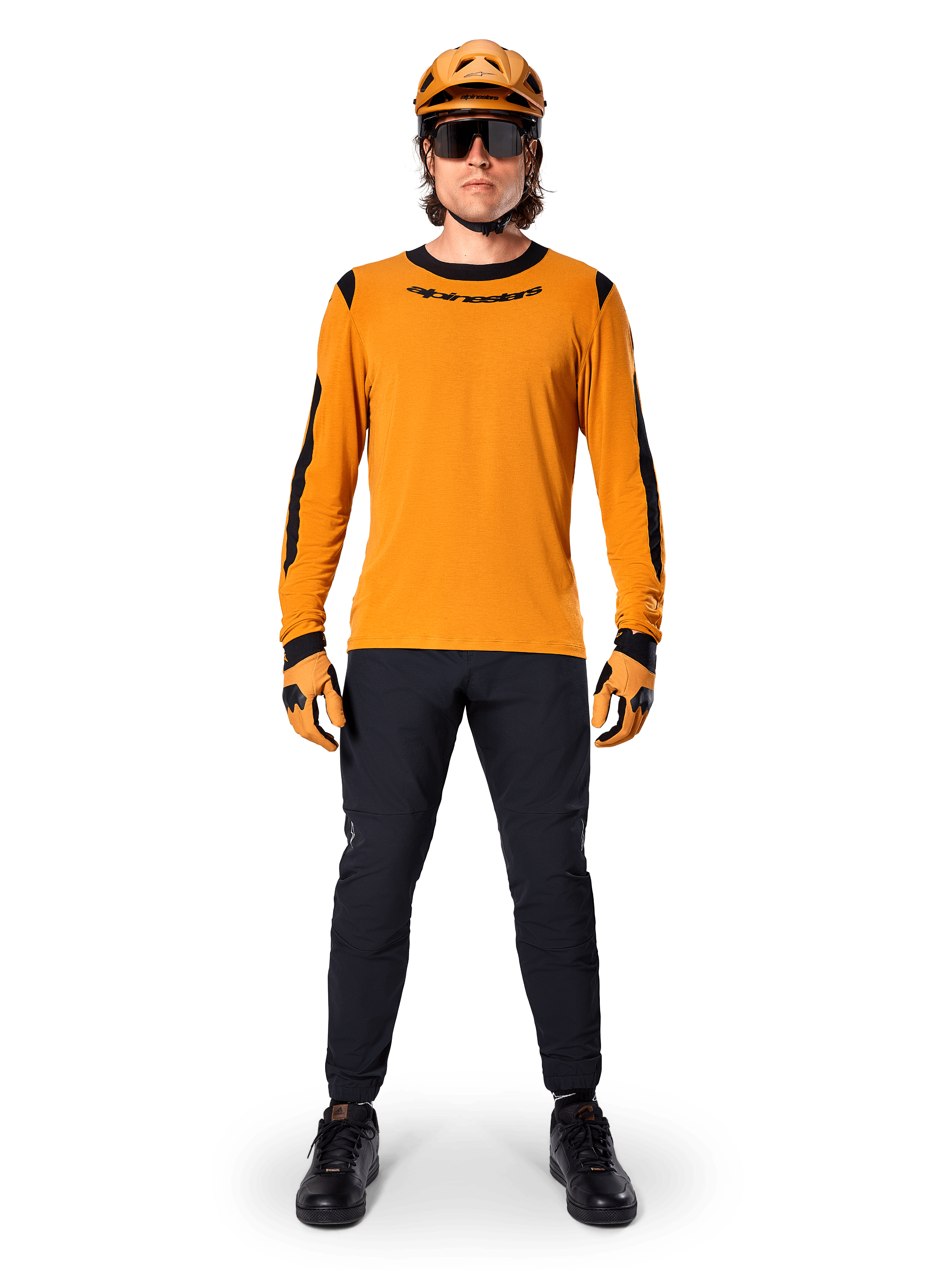 Mountainbiker met Alpinestars A-Dura Dri Wool jersey met lange mouwen, donkergoud met zwarte accenten op de kraag en mouwen, gecombineerd met een zwarte broek, bijpassende gouden helm, handschoenen en zwarte zonnebril, professionele mountainbike-uitrusting