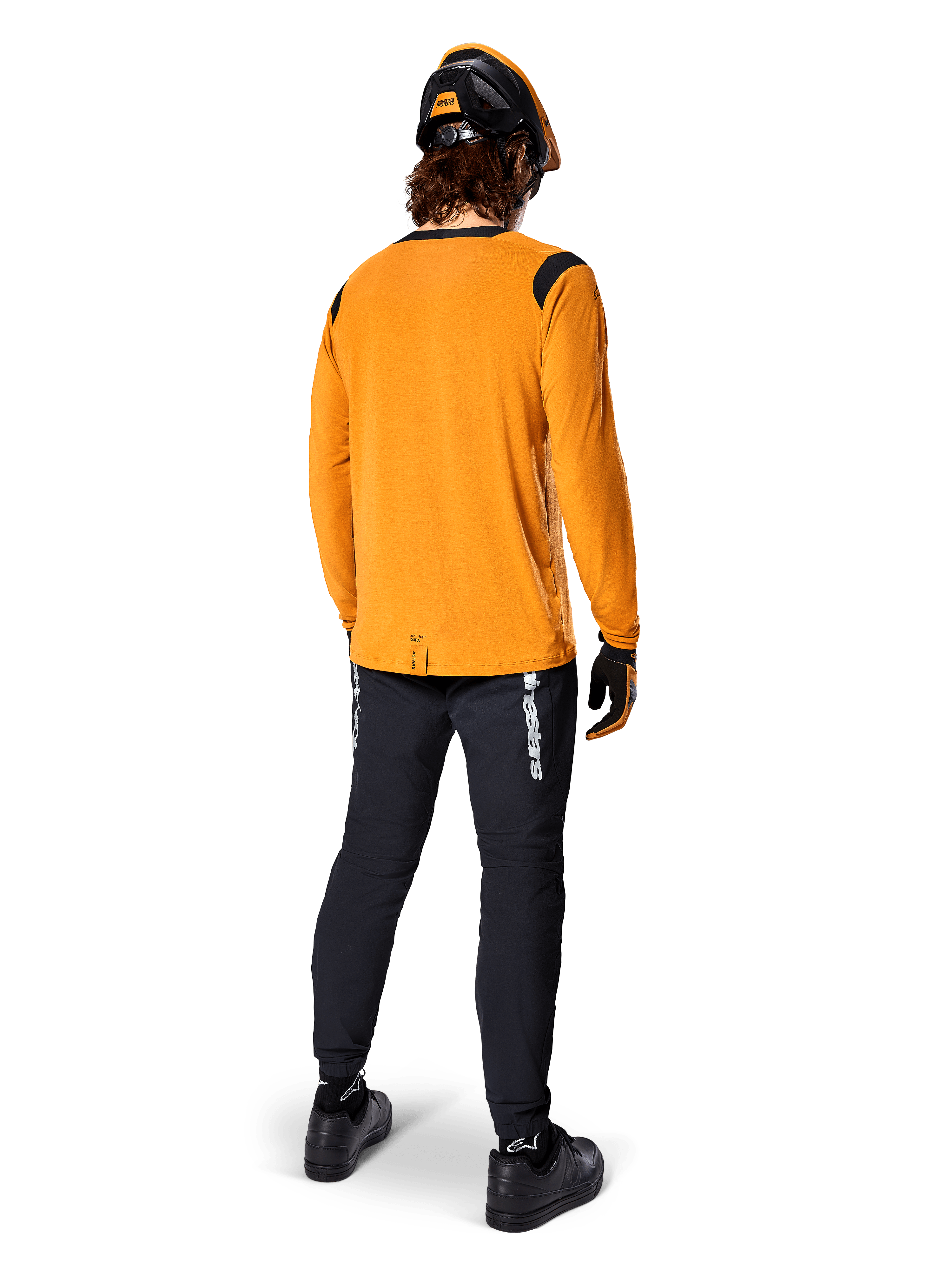 Mountainbiker van achteren gezien, dragend het Alpinestars A-Dura Dri Wool Jersey met lange mouwen in Dark Gold, zwarte technische broek met witte logo's en een bijpassende zwart-oranje helm, prestatiegerichte mountainbikekleding.