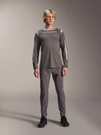 Alpinestars A-Dura Dri Wool Jersey met lange mouwen, donkergrijs, gedragen door model met bijpassende grijze broek en zwarte schoenen, witte Alpinestars-branding op de borst, lichtgrijze mesh-panelen op de schouders en mouwen, technische mountainbike-kleding