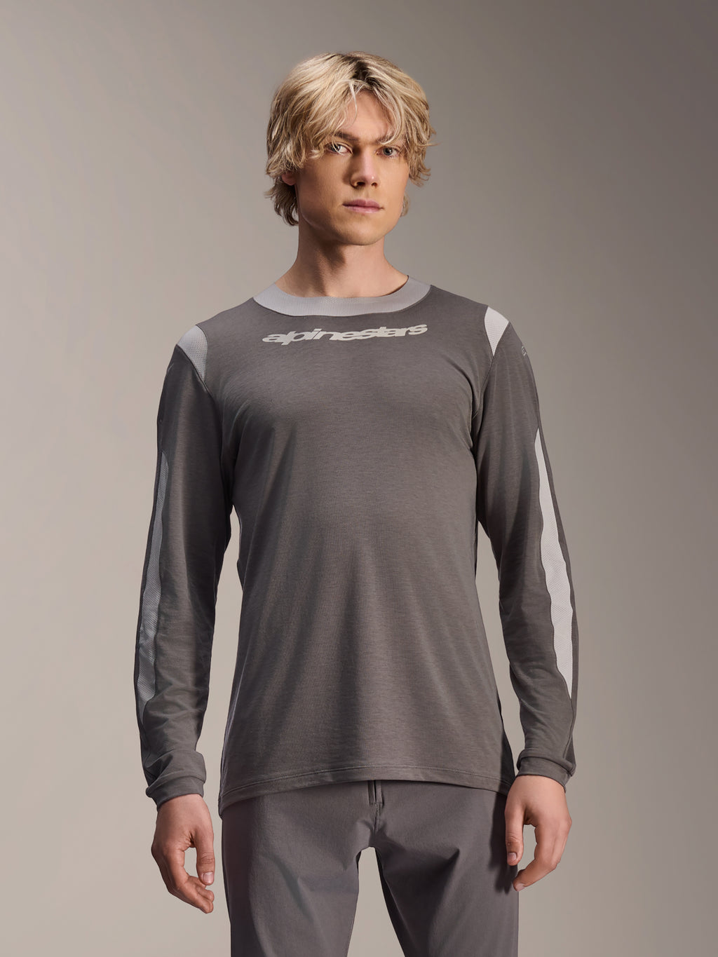 Alpinestars A-Dura Dri Wool Jersey met lange mouwen, donkergrijs, gedragen door een mannelijk model, voorzien van lichtgrijze mesh-panelen op de schouders en mouwen, wit logo op de borst, technische mountainbike-uitrusting