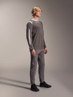 Mannelijk model draagt Alpinestars A-Dura Dri Wool Jersey met lange mouwen in donkergrijs, gecombineerd met bijpassende grijze broek en zwarte schoenen, voorzien van lichtgrijze mesh-panelen op de schouders en mouwen, technische MTB-uitrusting voor off-road fietsen