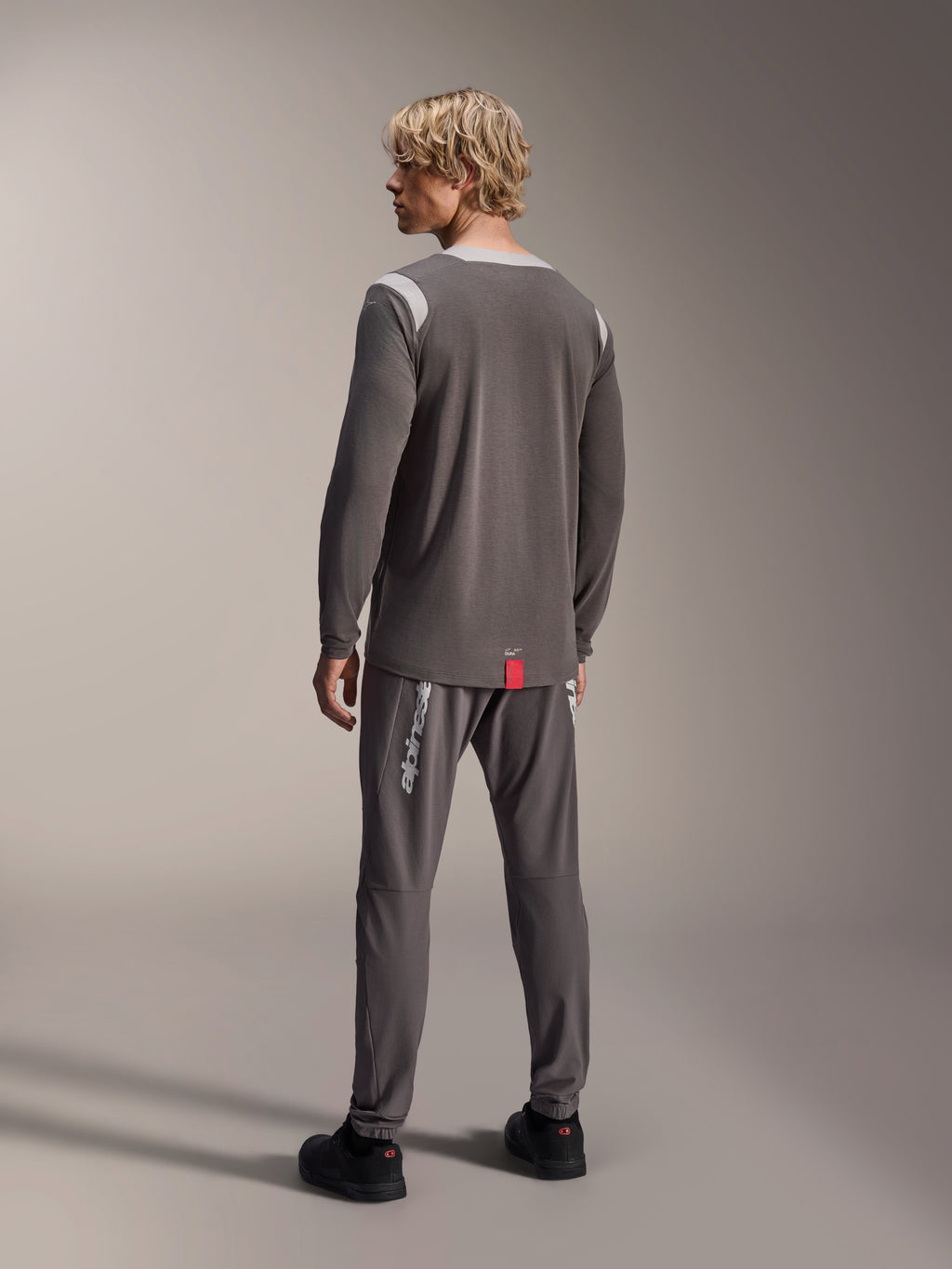 Alpinestars A-Dura Dri Wool Long Sleeve Jersey, donkergrijs met lichtgrijze mesh schouderpanelen, gecombineerd met bijpassende donkergrijze fietsbroek, achteraanzicht met de verlengde achterzoom, mountainbike-kleding