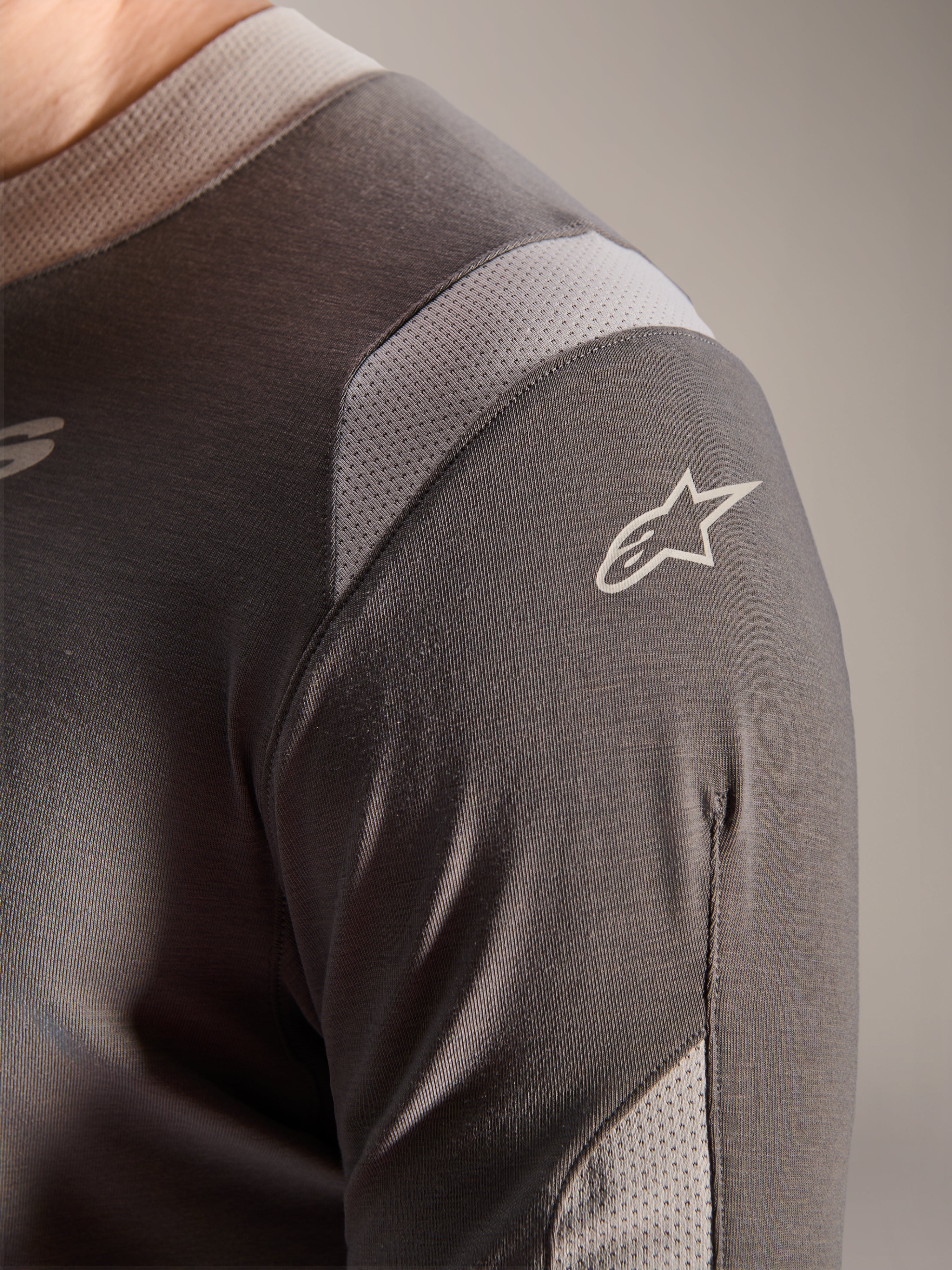 Alpinestars A-Dura Dri Wool Jersey - Lange Mouwen, donkergrijs, detailopname van de schouder en mouw met lichtgrijze mesh ventilatiepanelen en het witte Astars-logo op de technische drirelease-stof.