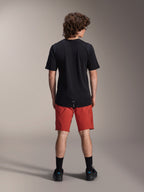 Männliches Model in Alpinestars A-Dura Elite Shorts in Dark Orange und schwarzem A-Dura Dri Wool Kurzarmtrikot, Rückansicht, kombiniert mit schwarzen Socken und Fahrradschuhen, professionelle Mountainbike-Bekleidung