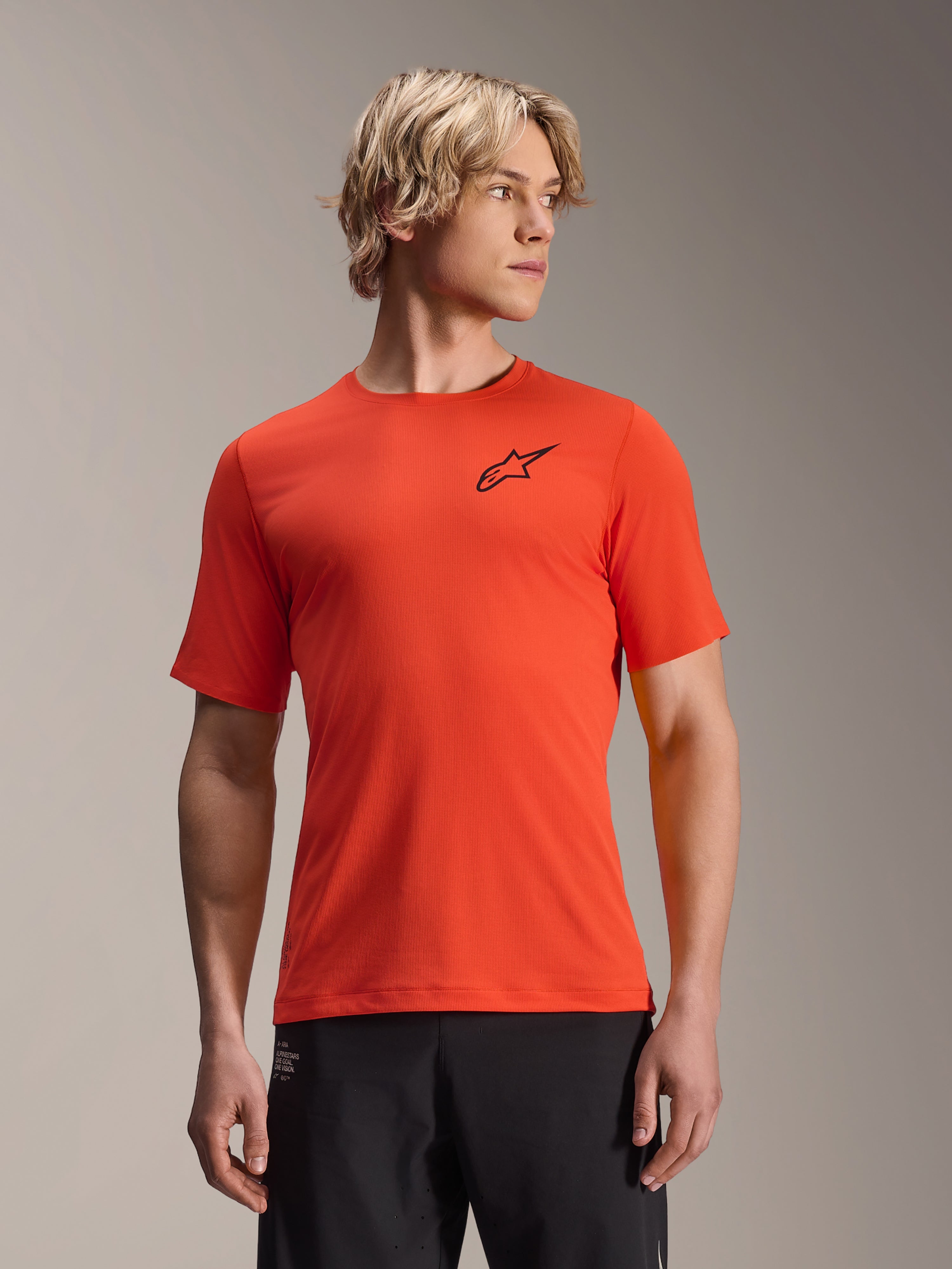Alpinestars A-Aria Astar Kurzarm-Trikot, Spicy Orange mit schwarzem Stern-Logo, Herren-MTB-Mountainbike-Jersey, Performance-Passform, getragen von männlichem Model mit blondem Haar und schwarzer Hose