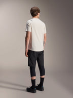 Alpinestars A-Aria Astar Jersey, MTB-shirt met korte mouwen, Ecru, achteraanzicht dat de prestatiegerichte pasvorm en verlengde achterzijde toont, gecombineerd met een zwarte mountainbike short, kniebeschermers en zwarte fietsschoenen voor off-road trailsessies