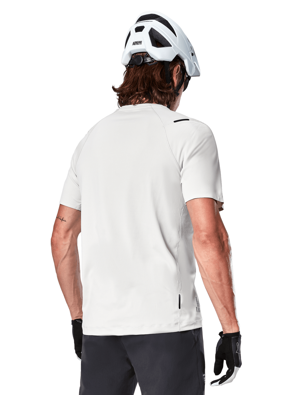 Alpinestars A-Aria Astar Jersey, manches courtes, White Dove, vue arrière d'un maillot de VTT léger et respirant, porté avec un casque blanc et des gants de cyclisme noirs, doté d'un pan arrière plus long pour une couverture accrue
