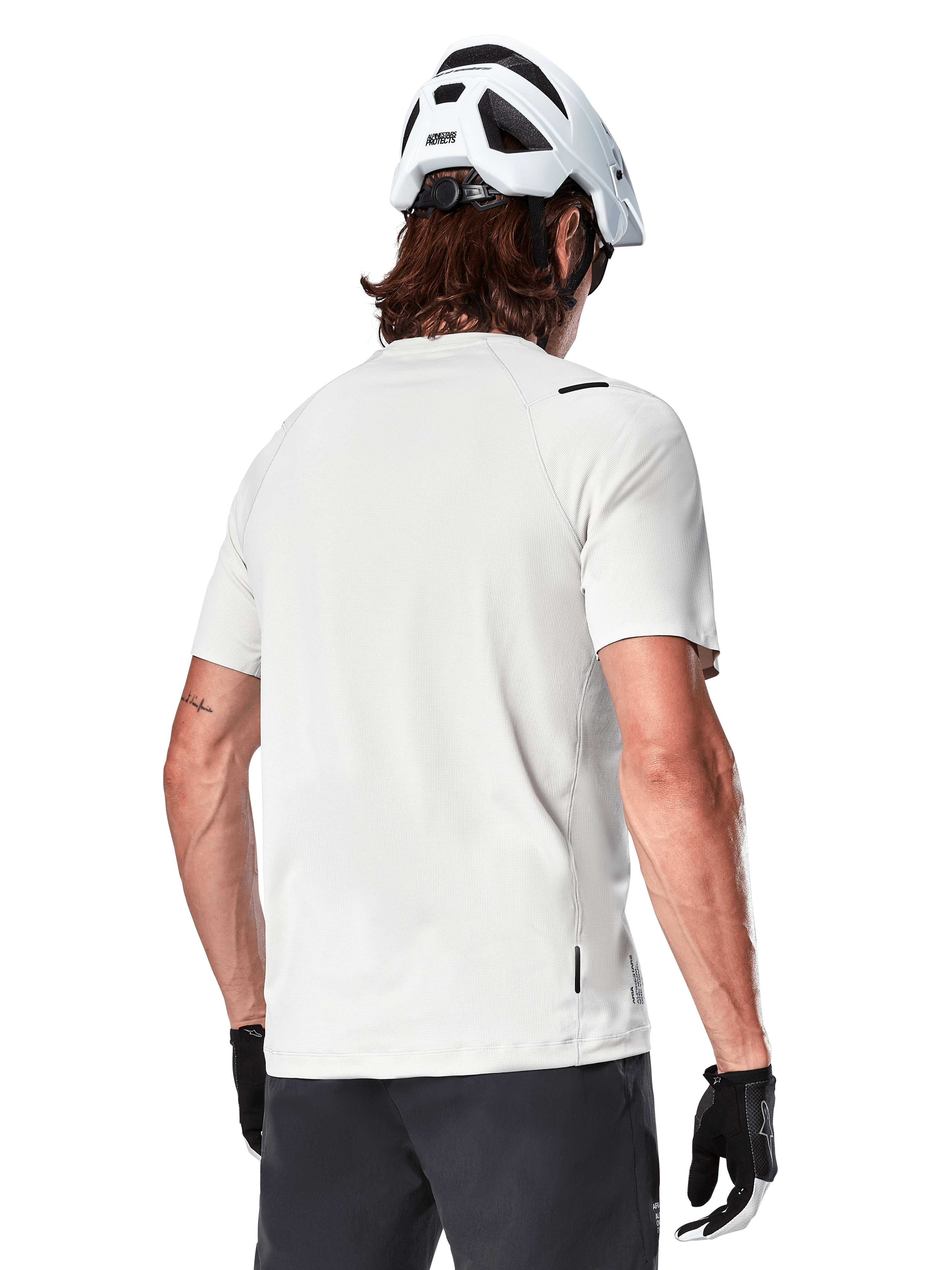 Alpinestars A-Aria Astar Jersey, manches courtes, White Dove, vue arrière d'un maillot de VTT léger et respirant, porté avec un casque blanc et des gants de cyclisme noirs, doté d'un pan arrière plus long pour une couverture accrue