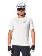 Cycliste portant le maillot à manches courtes Alpinestars A-Aria Astar, White Dove avec petit logo Astar noir sur la poitrine, casque de cyclisme blanc, lunettes de soleil noires et gants noirs et blancs, équipement VTT performant pour la conduite tout-terrain