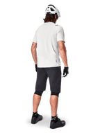 Cycliste portant le maillot à manches courtes Alpinestars A-Aria Astar en White Dove, vue arrière, associé à un short de VTT noir, des genouillères et un casque blanc, équipement léger et respirant pour le VTT tout-terrain