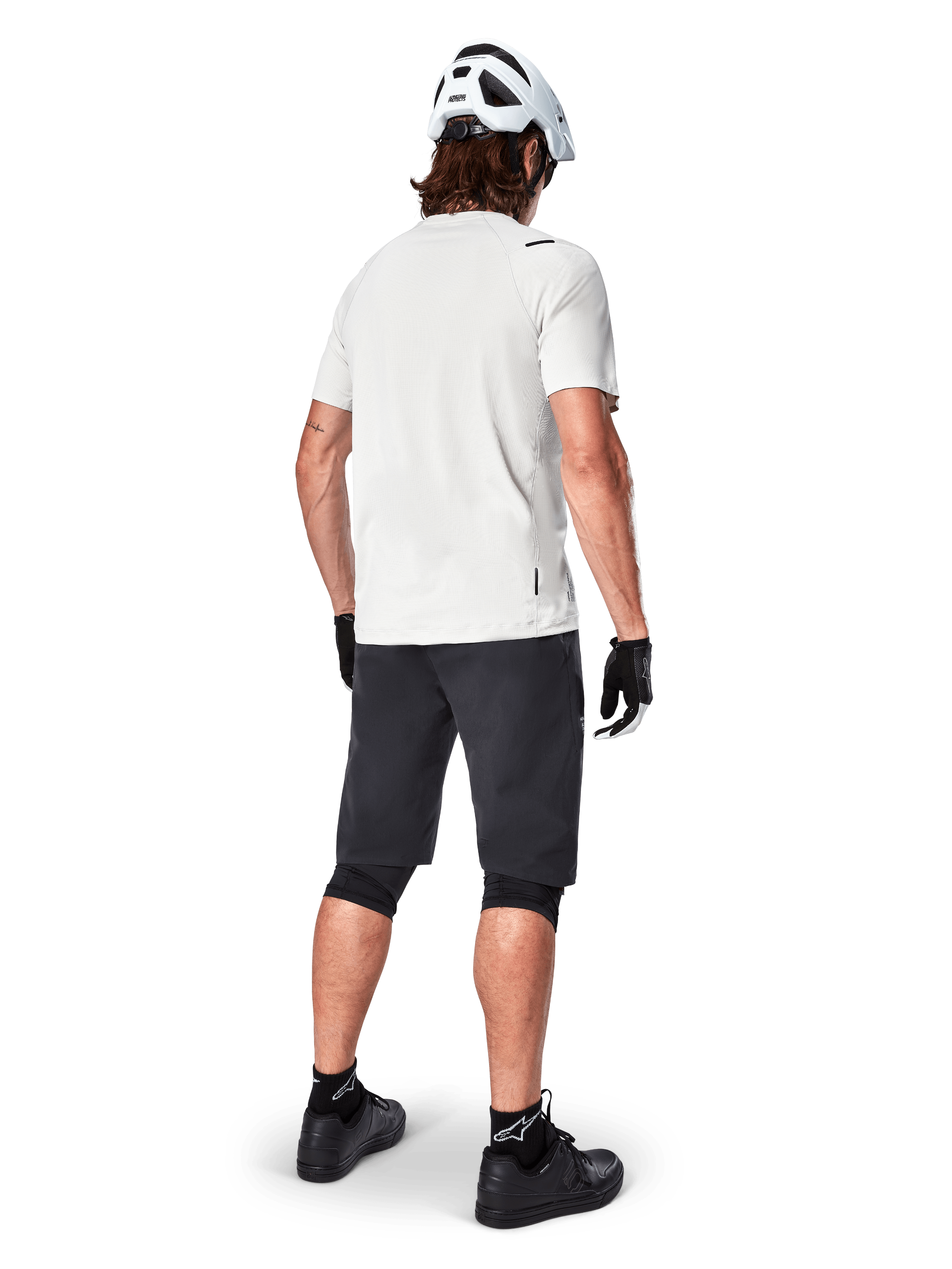Cycliste portant le maillot à manches courtes Alpinestars A-Aria Astar en White Dove, vue arrière, associé à un short de VTT noir, des genouillères et un casque blanc, équipement léger et respirant pour le VTT tout-terrain