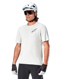 Maillot à manches courtes Alpinestars A-Aria Astar, White Dove, porté par un cycliste avec un casque blanc et des lunettes de soleil foncées, arborant un petit logo d'étoile noir sur la poitrine, équipement de performance respirant pour le VTT