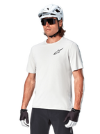 Maillot à manches courtes Alpinestars A-Aria Astar, White Dove, porté par un cycliste avec un casque blanc et des lunettes de soleil foncées, arborant un petit logo d'étoile noir sur la poitrine, équipement de performance respirant pour le VTT