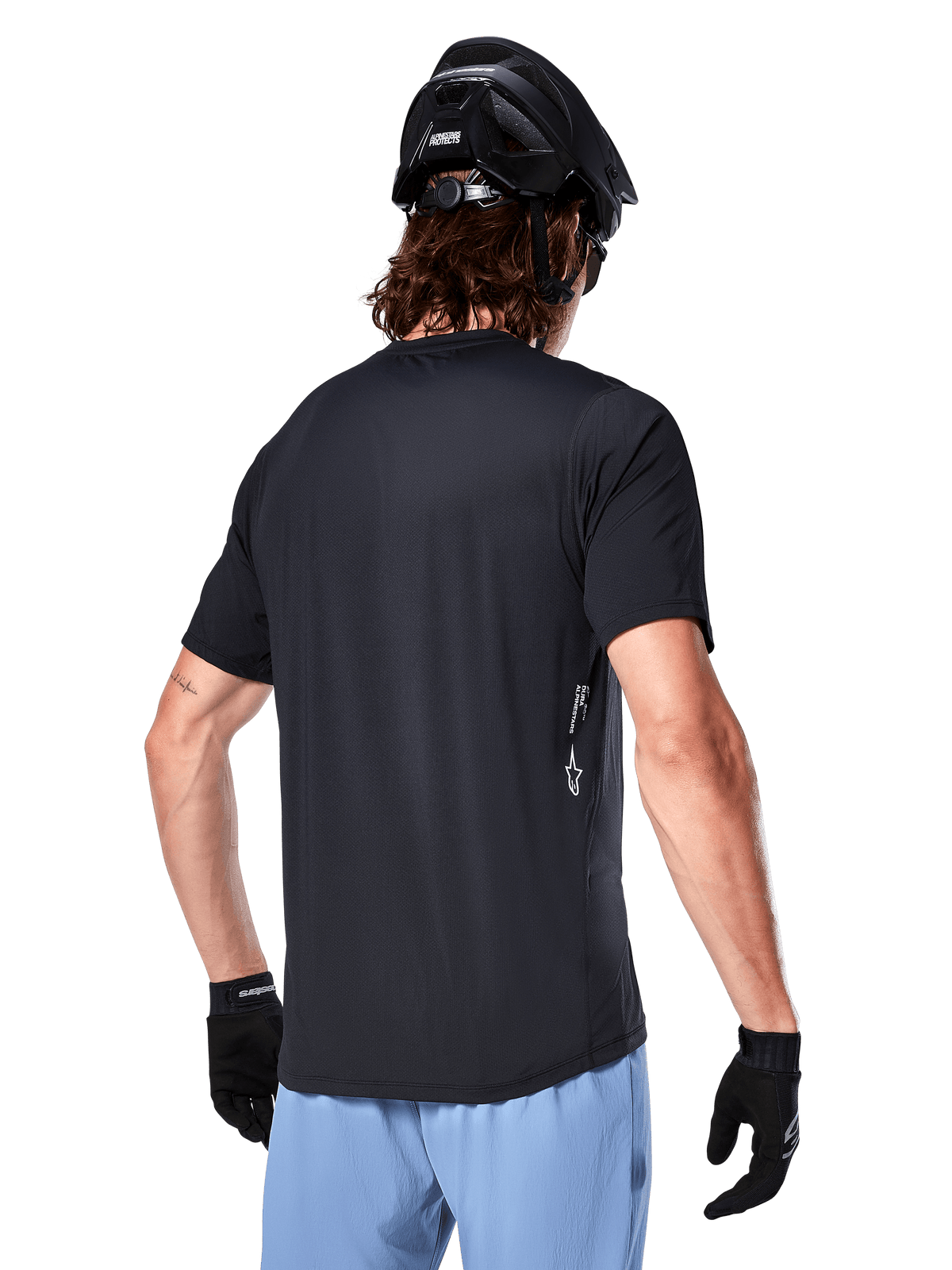 Alpinestars A-Dura Oscar Jersey, fietsshirt met korte mouwen, zwart, achteraanzicht op de rijder, gecombineerd met een lichtblauwe short en zwarte MTB-helm, klein wit logo aan de zijkant, prestatiekleding voor mountainbiken