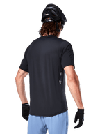 Alpinestars A-Dura Oscar Jersey, maillot de cyclisme à manches courtes, noir, vue de dos sur un cycliste, associé à un short bleu clair et un casque VTT noir, petit logo blanc sur le côté, vêtement de performance pour le VTT