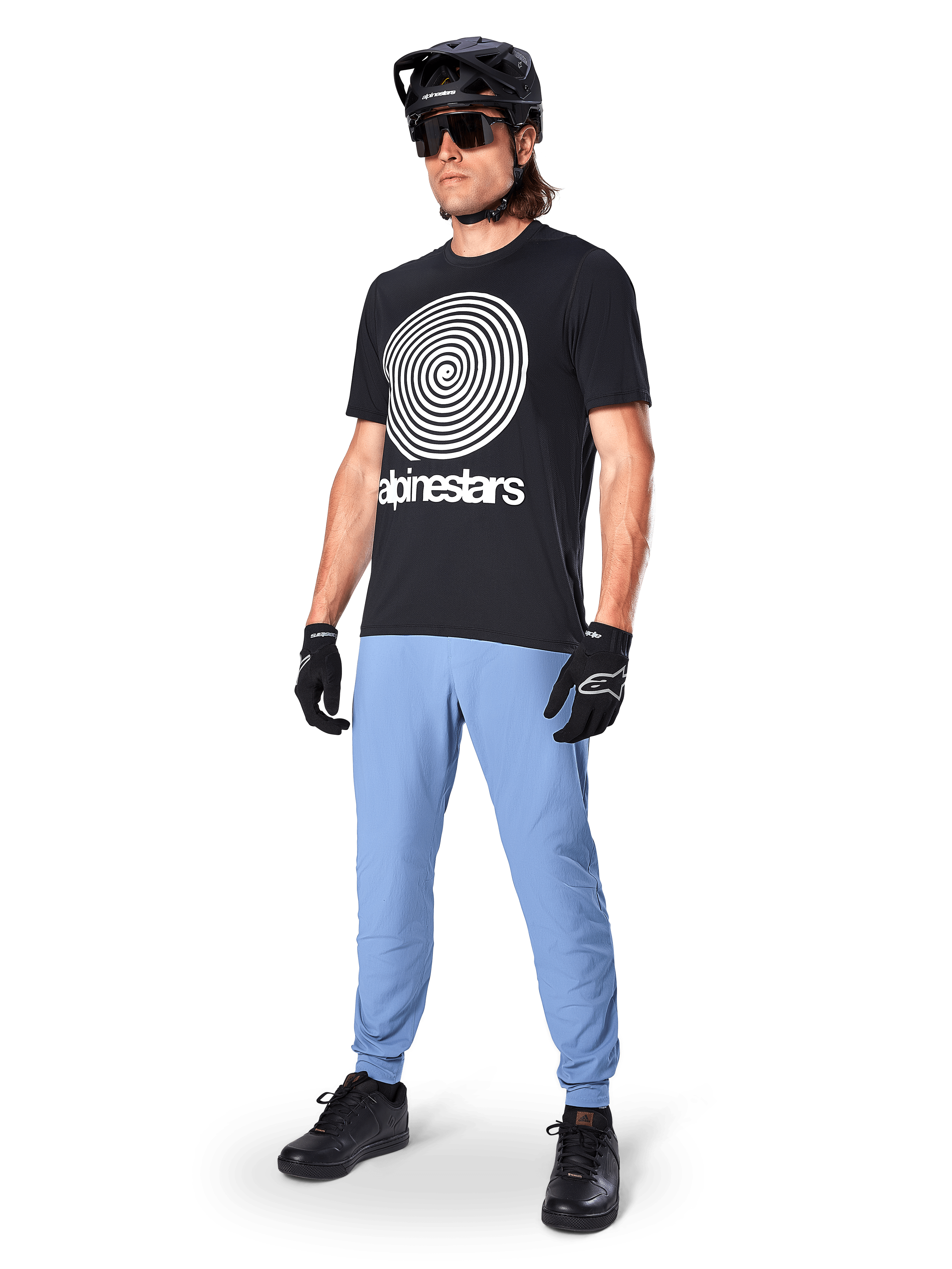 Maillot à manches courtes Alpinestars A-Dura Oscar, maillot de VTT noir avec un grand graphique en spirale blanc vintage, porté par un cycliste avec un casque noir, des lunettes de soleil, des gants noirs et un pantalon bleu clair, équipement de VTT haute performance