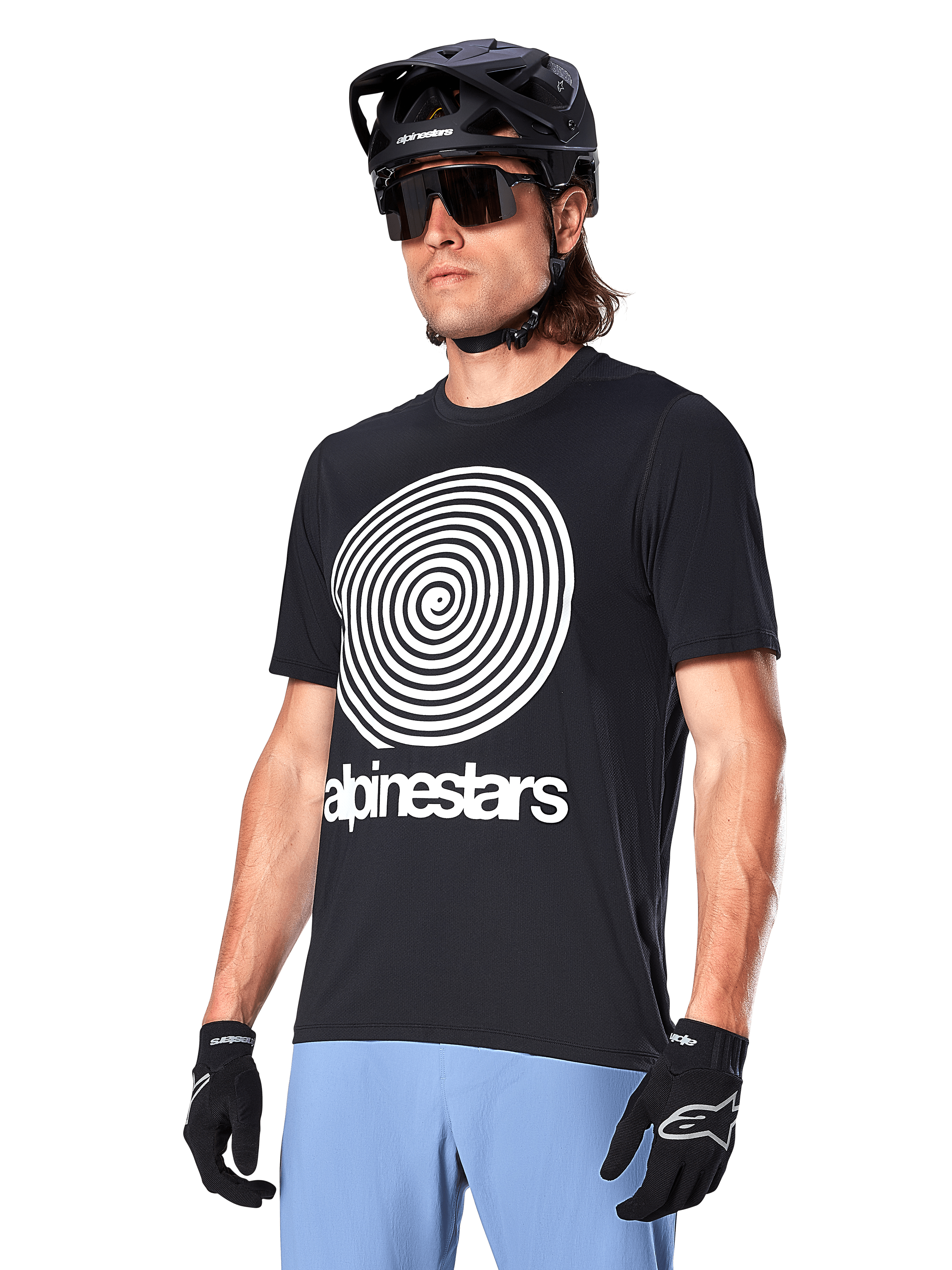 Alpinestars A-Dura Oscar Jersey - korte mouwen, zwart, met een grote witte spiraalgrafiek en Alpinestars-logo op de borst, gedragen door een rijder met een zwarte MTB-helm, zonnebril en lichtblauwe broek