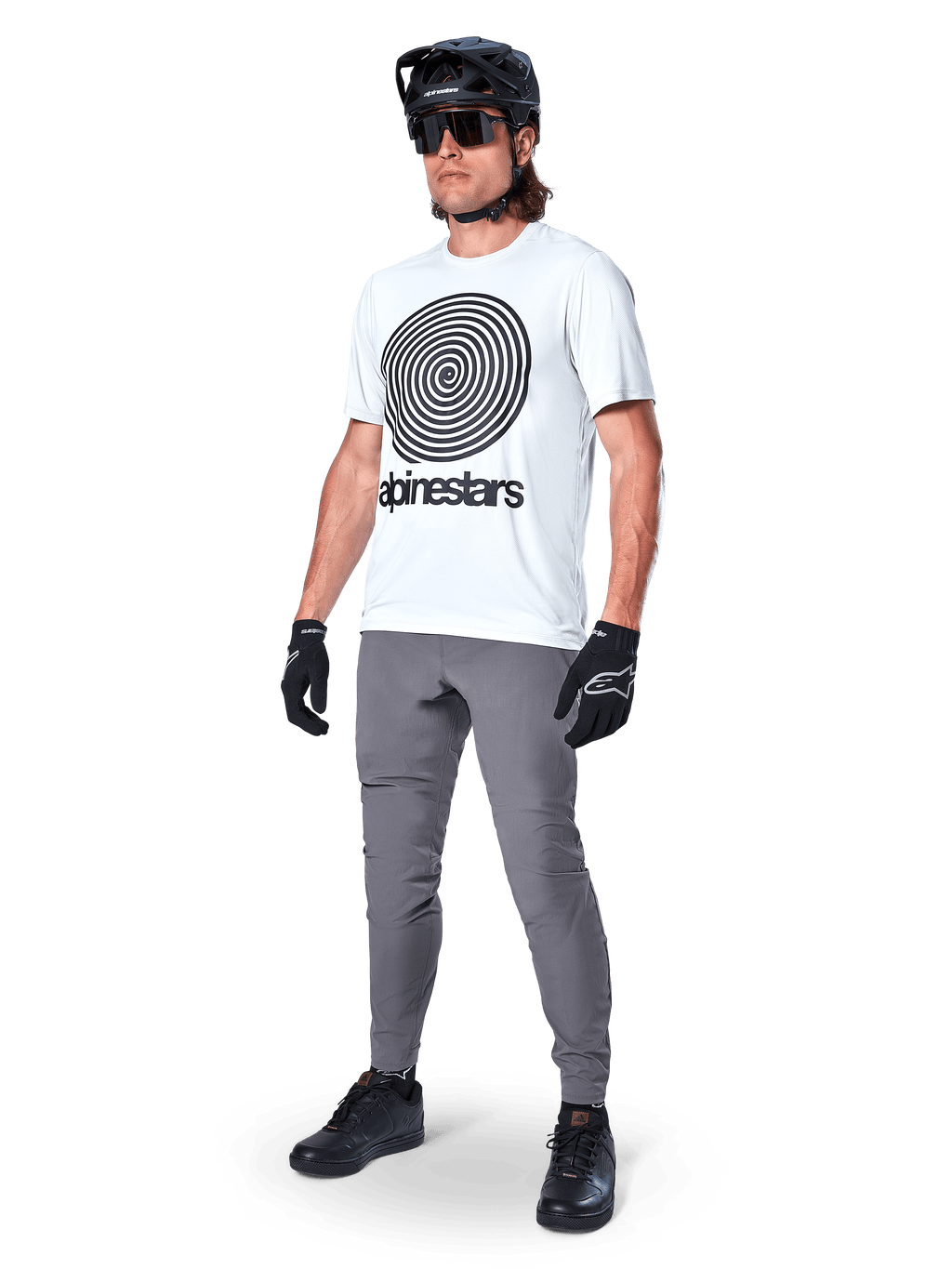 Maillot à manches courtes Alpinestars A-Dura Oscar, blanc White Dove avec grand graphique en spirale noire, porté par un cycliste avec pantalon de VTT gris, casque noir et gants, équipement de cyclisme de performance pour le tout-terrain