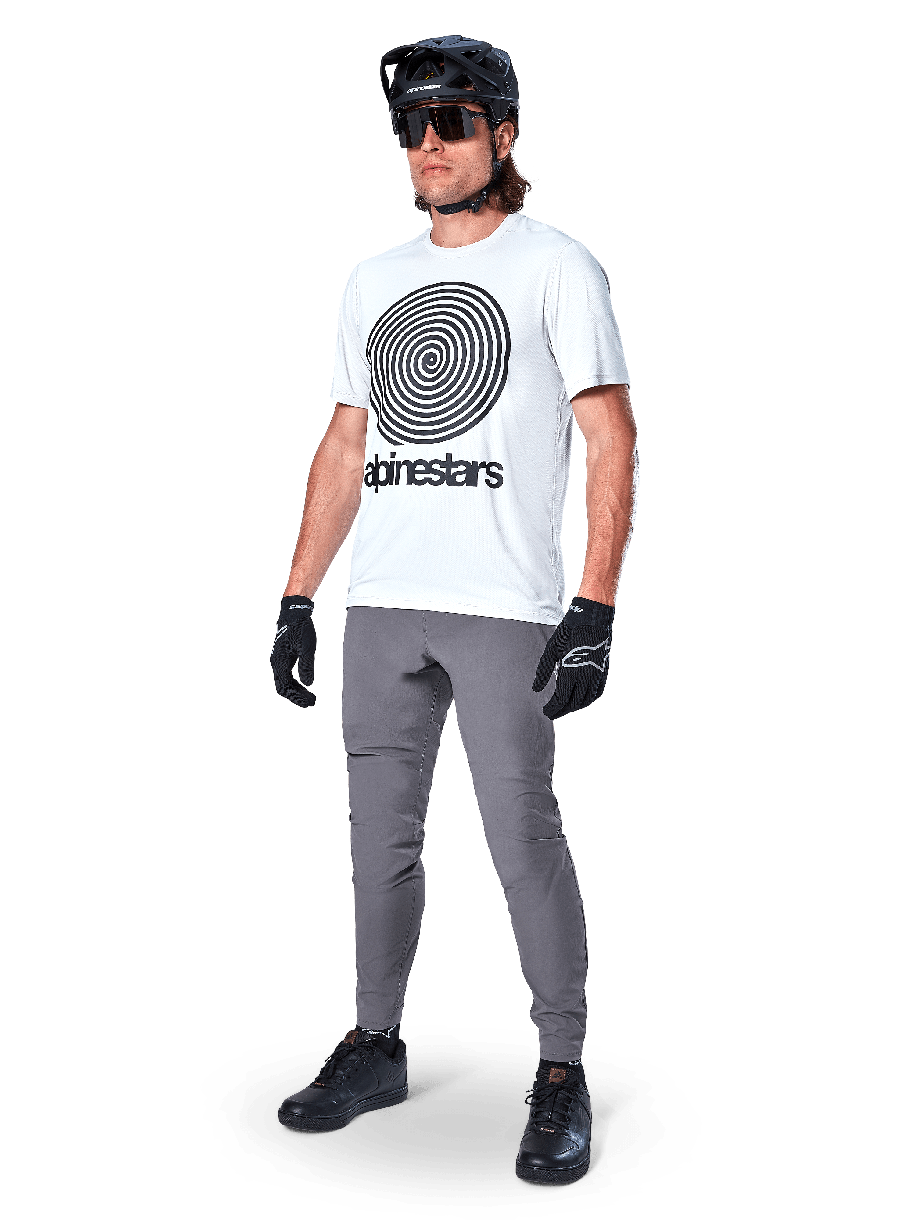 Maillot à manches courtes Alpinestars A-Dura Oscar, blanc White Dove avec grand graphique en spirale noire, porté par un cycliste avec pantalon de VTT gris, casque noir et gants, équipement de cyclisme de performance pour le tout-terrain