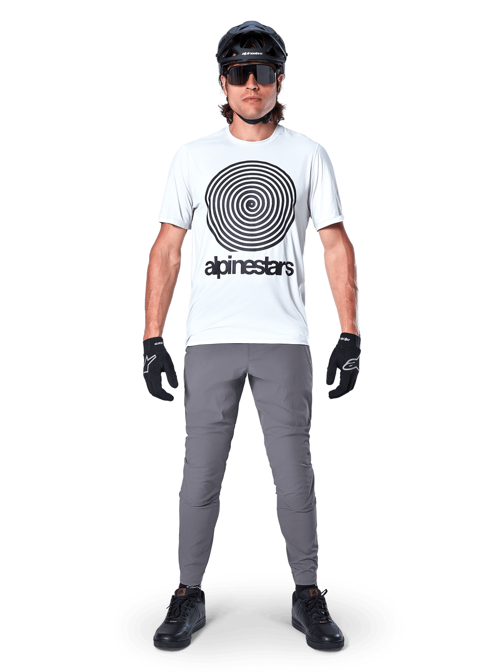 Vététiste portant le maillot Alpinestars A-Dura Oscar à manches courtes, White Dove avec un grand logo spirale noir, associé à un pantalon gris, un casque noir, des lunettes de soleil et des gants noirs, équipement de VTT haute performance