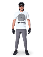 Vététiste portant le maillot Alpinestars A-Dura Oscar à manches courtes, White Dove avec un grand logo spirale noir, associé à un pantalon gris, un casque noir, des lunettes de soleil et des gants noirs, équipement de VTT haute performance